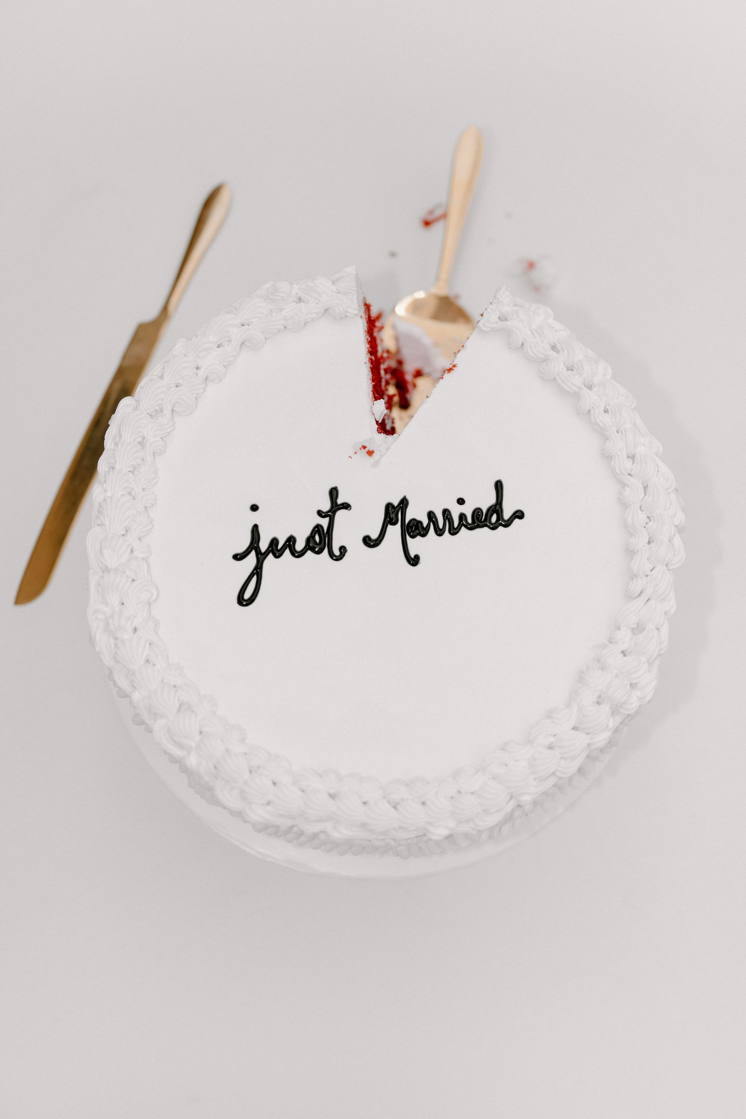 Top view of a white wedding cake with Just Married written in black script with gold cake servers.