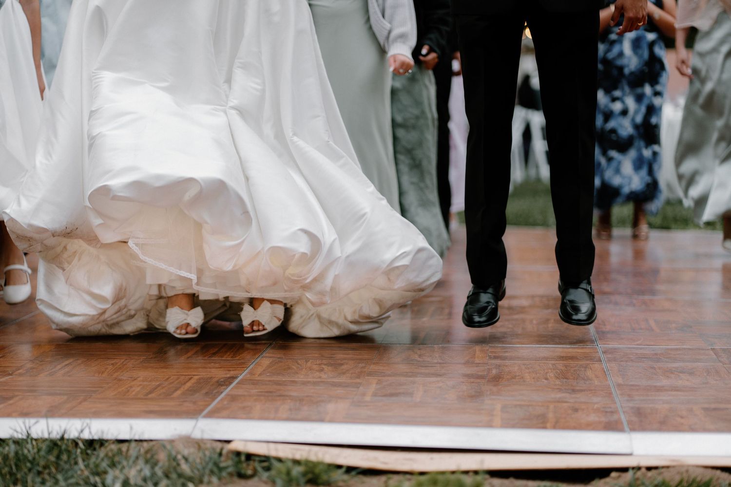 Close-up of bride and groom walking on wooden dance floor, bride wearing white heels under flowing gown.