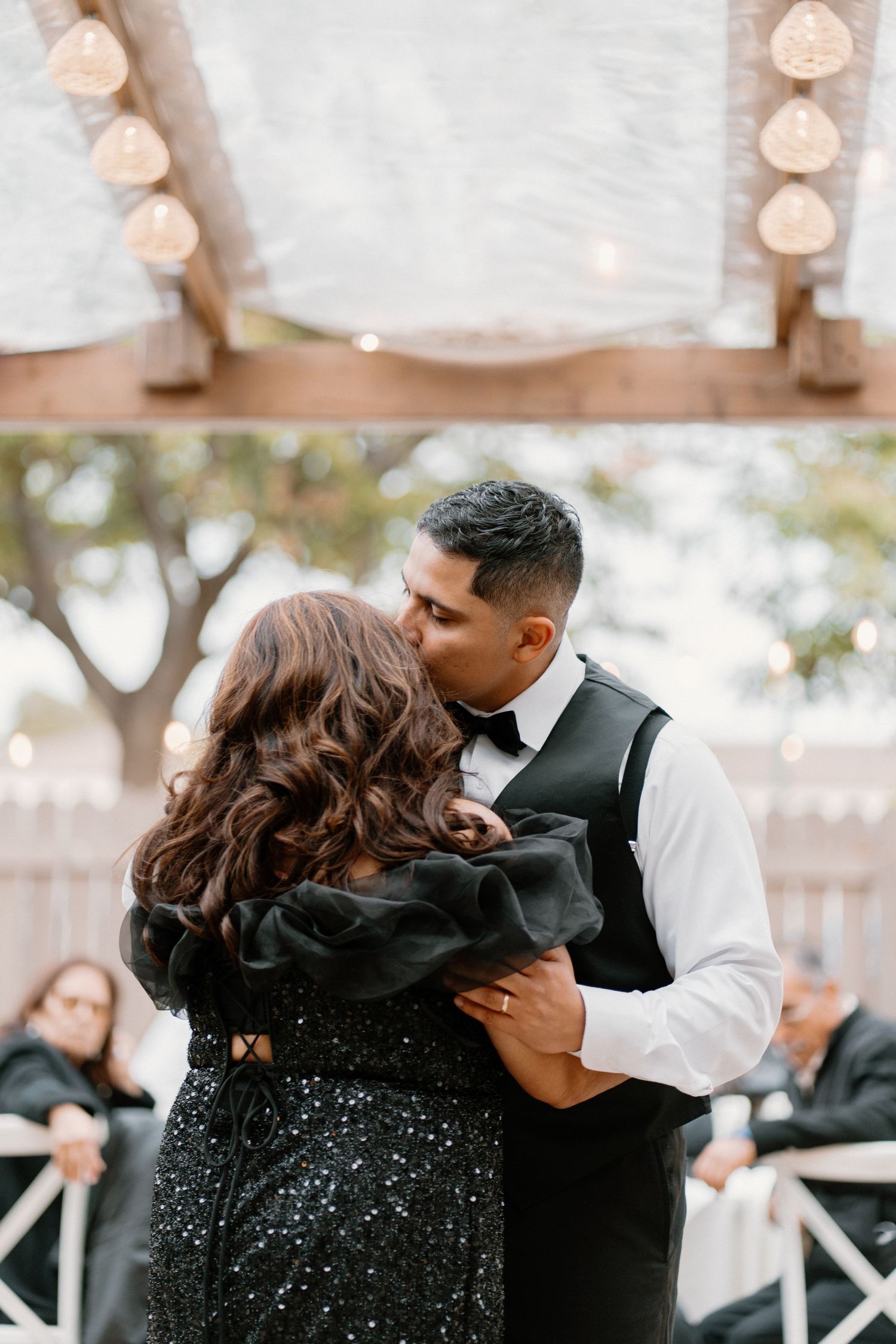 Groom sharing tender kiss with mother during special mother son dance at outdoor wedding reception.