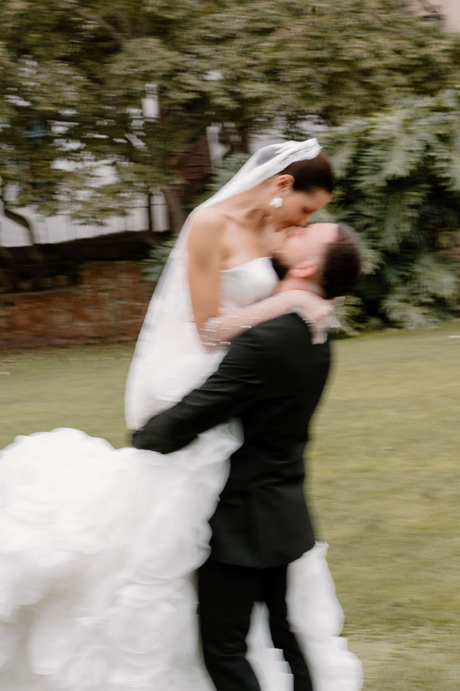 Groom lifting bride in white ballgown for a romantic kiss on a garden lawn.