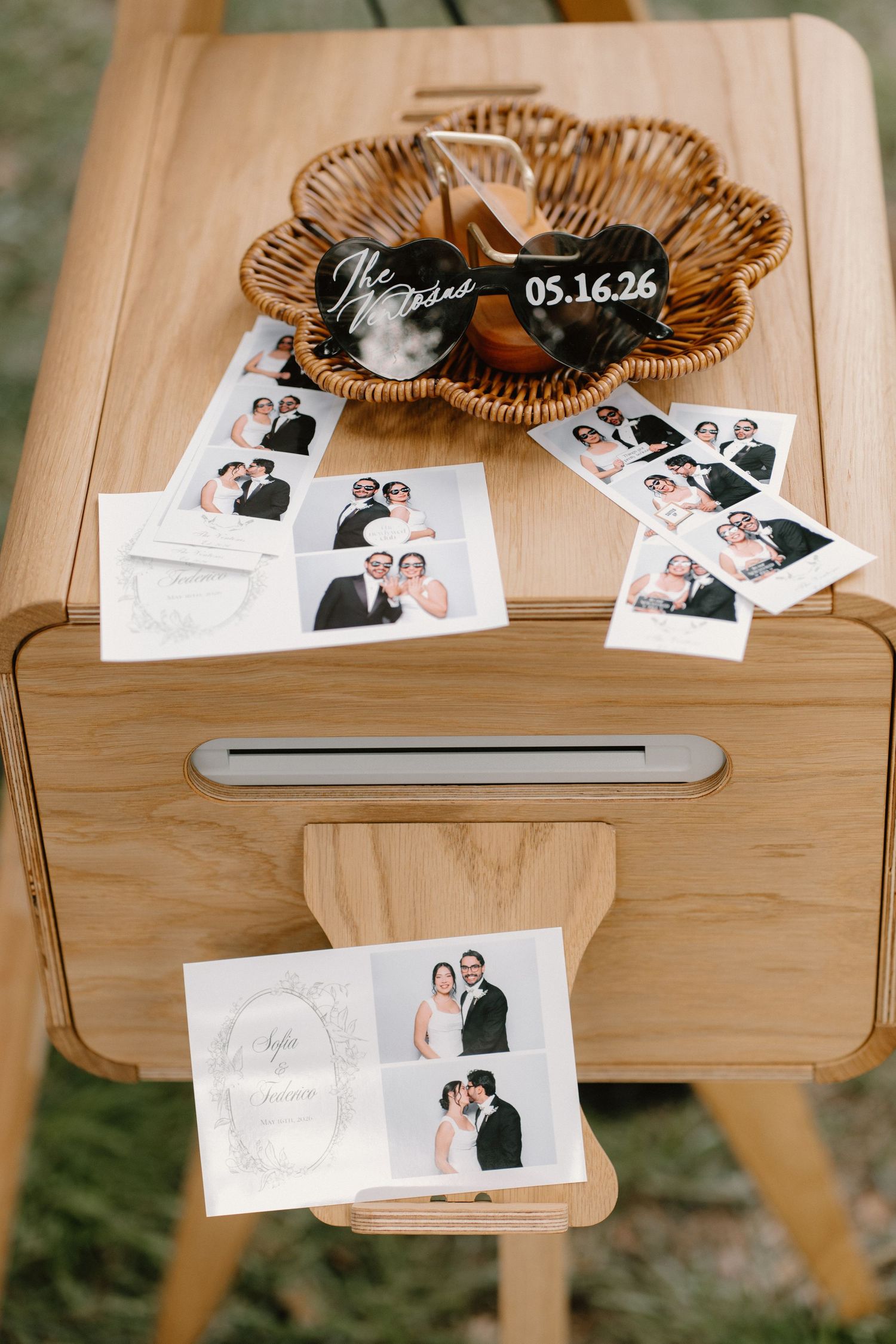 Wedding photo booth strips scattered on a wooden card box with personalized date magnets.