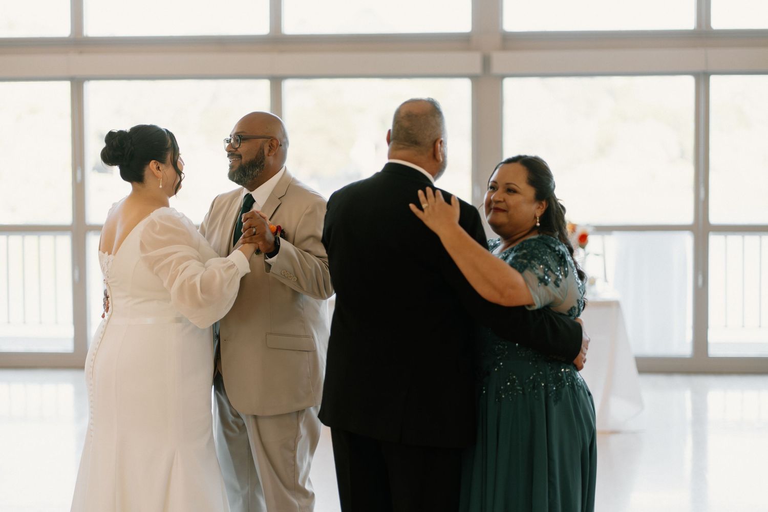 Two couples share a parent dance together in a bright reception hall during wedding.
