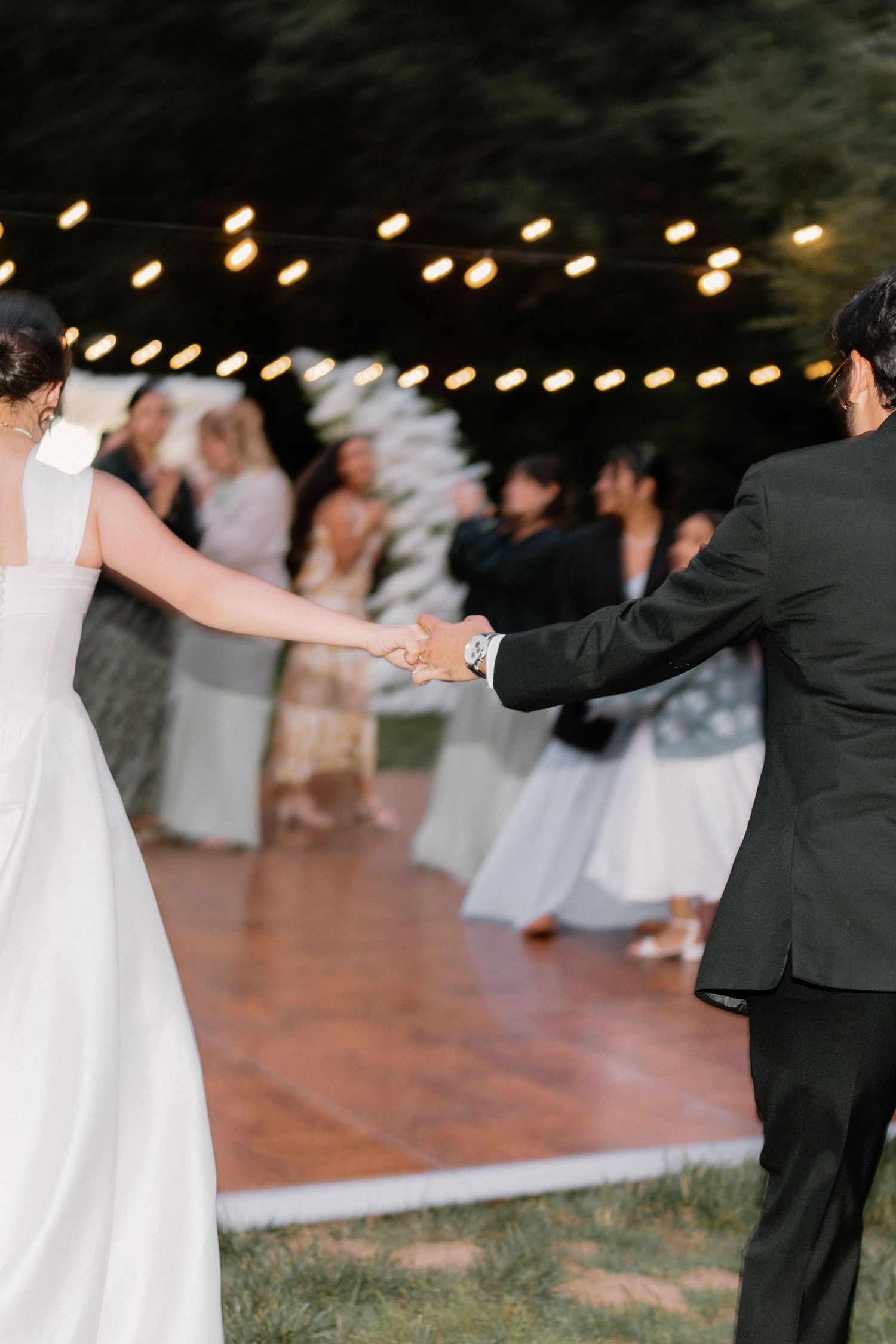 Bride and groom hold hands on wooden dance floor at elegant outdoor evening wedding.