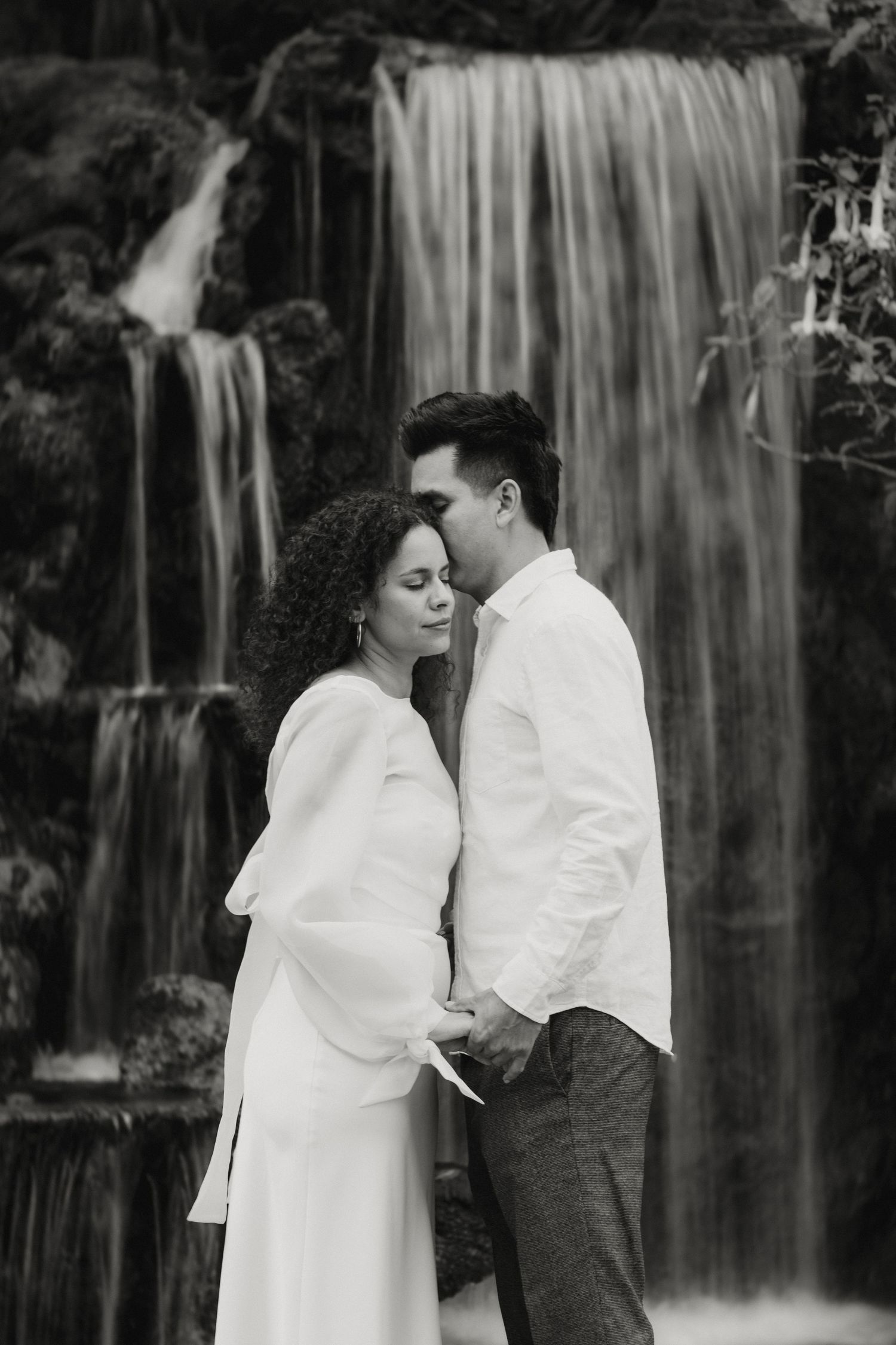 Black and white romantic photo of couple holding hands in front of a cascading waterfall.