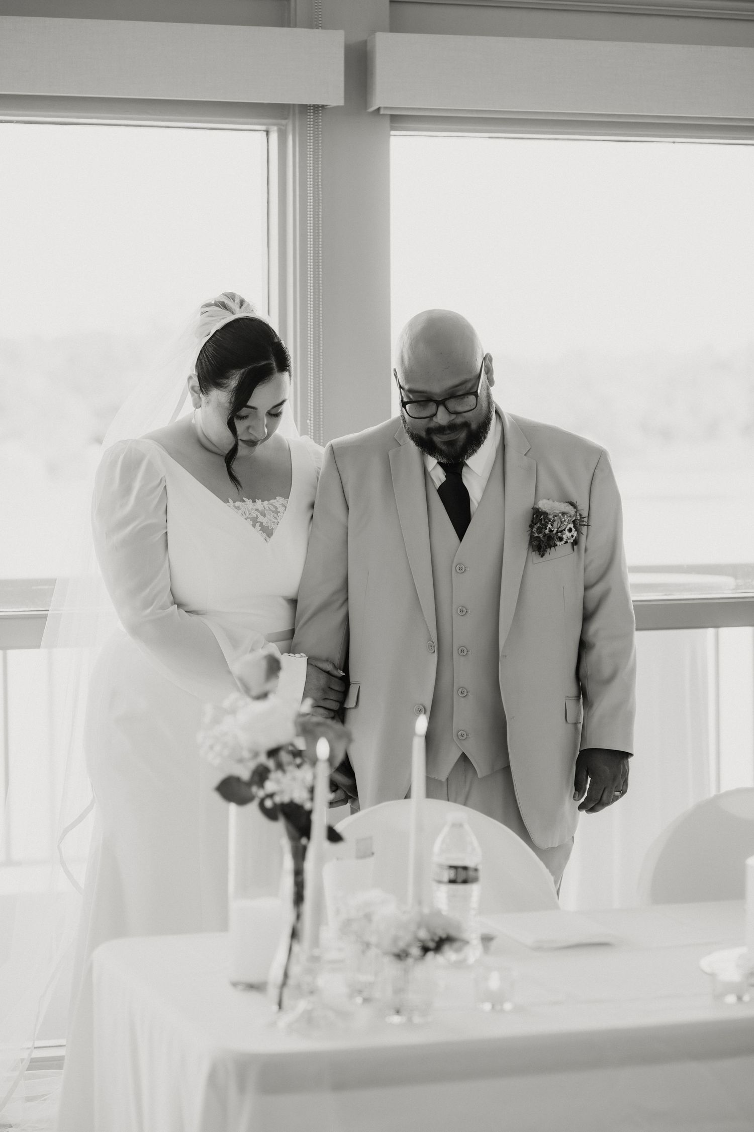 Black and white photo of bride and groom standing together at wedding ceremony table with candles.
