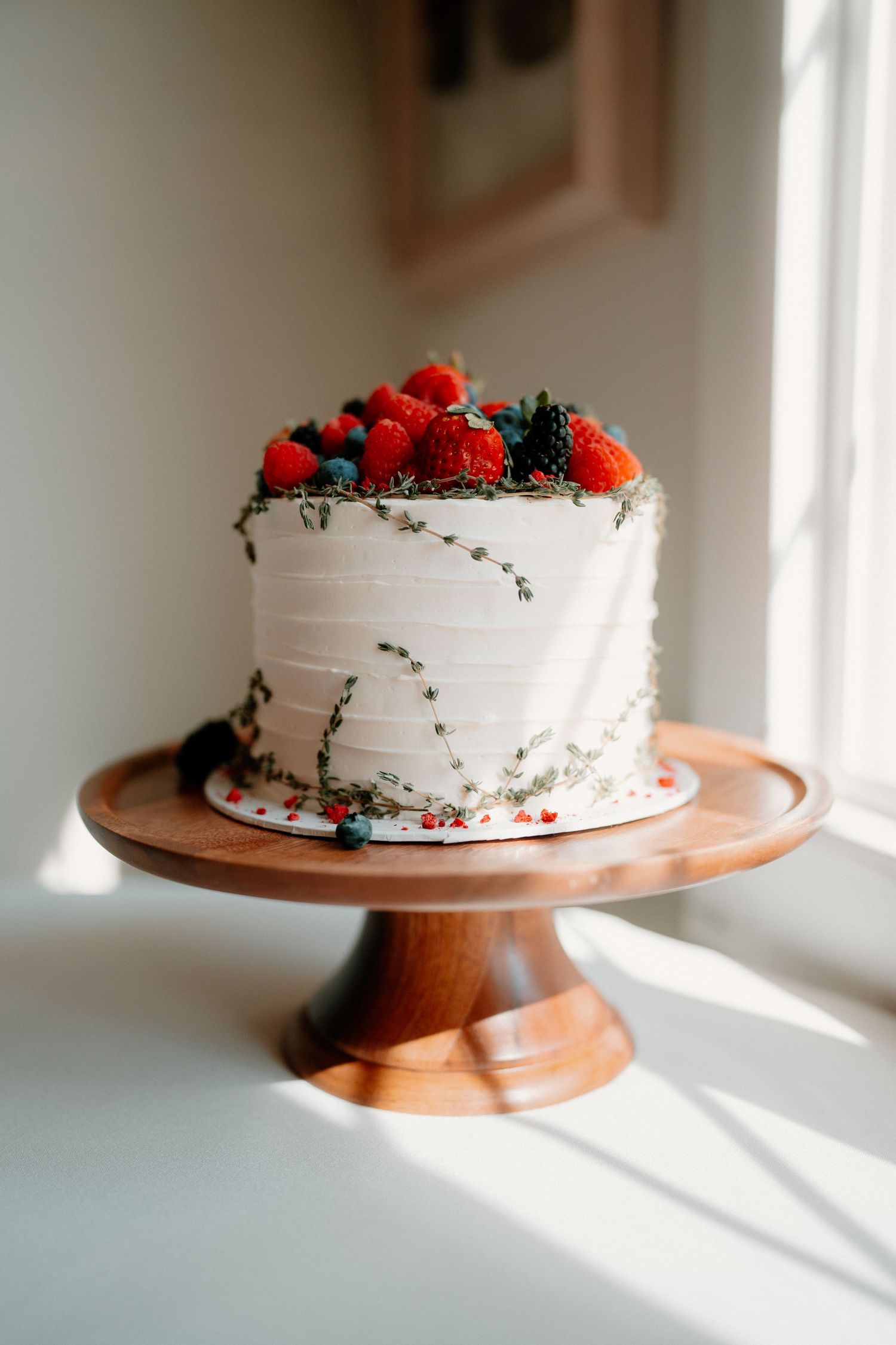 Elegant single-tier white wedding cake topped with fresh strawberries and berries on wooden cake stand.