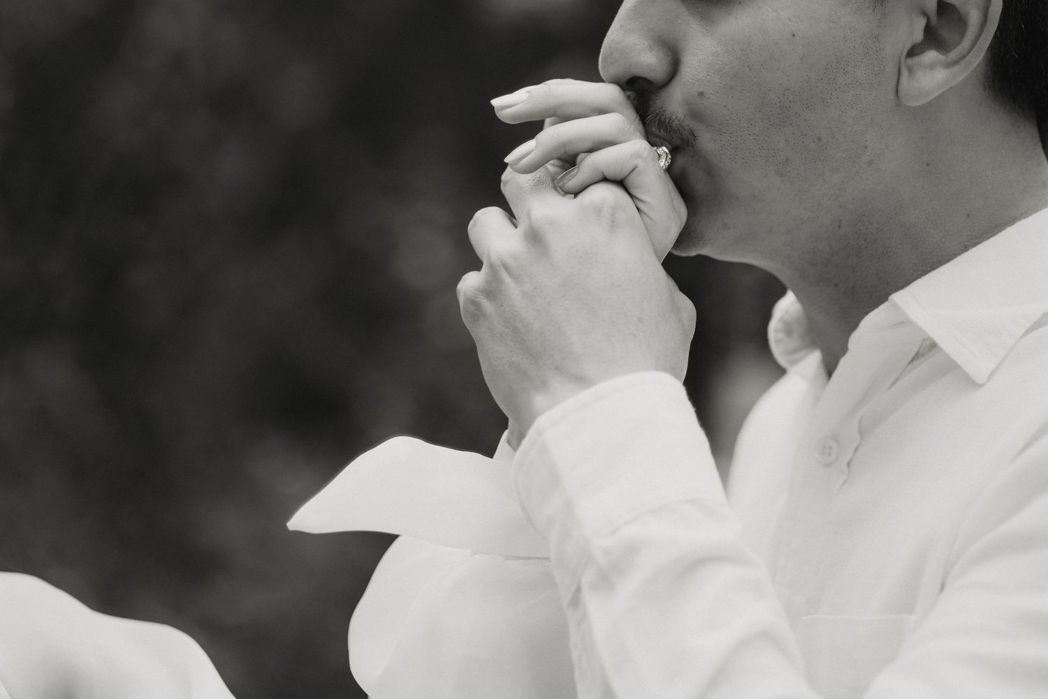 A groom in a white shirt tenderly kisses his bride's hand in a romantic black and white photo.