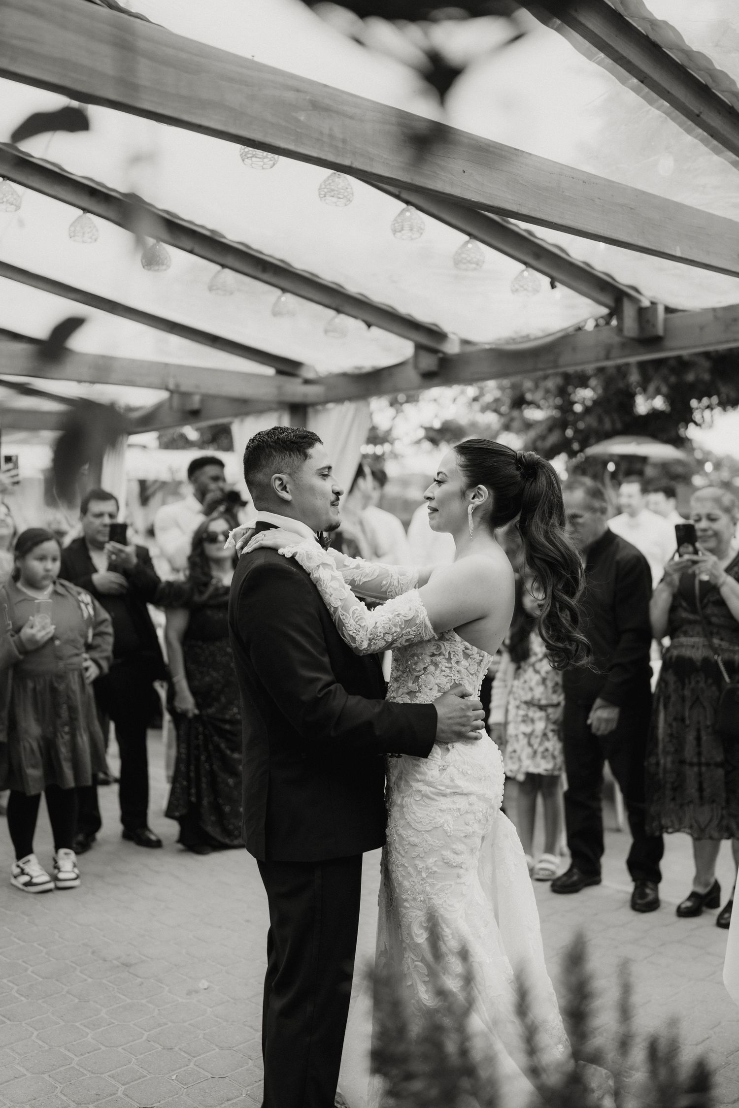 Black and white photo of bride and groom sharing their first dance surrounded by guests at outdoor reception.