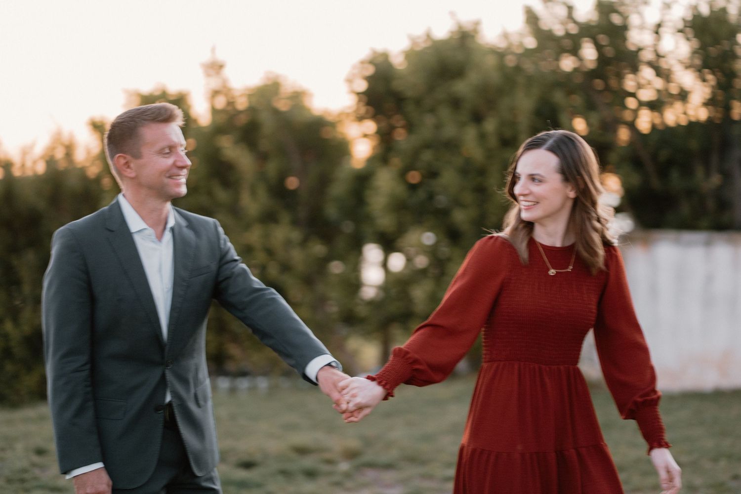 Happy engaged couple holding hands walking outdoors at golden hour in coordinating outfits.
