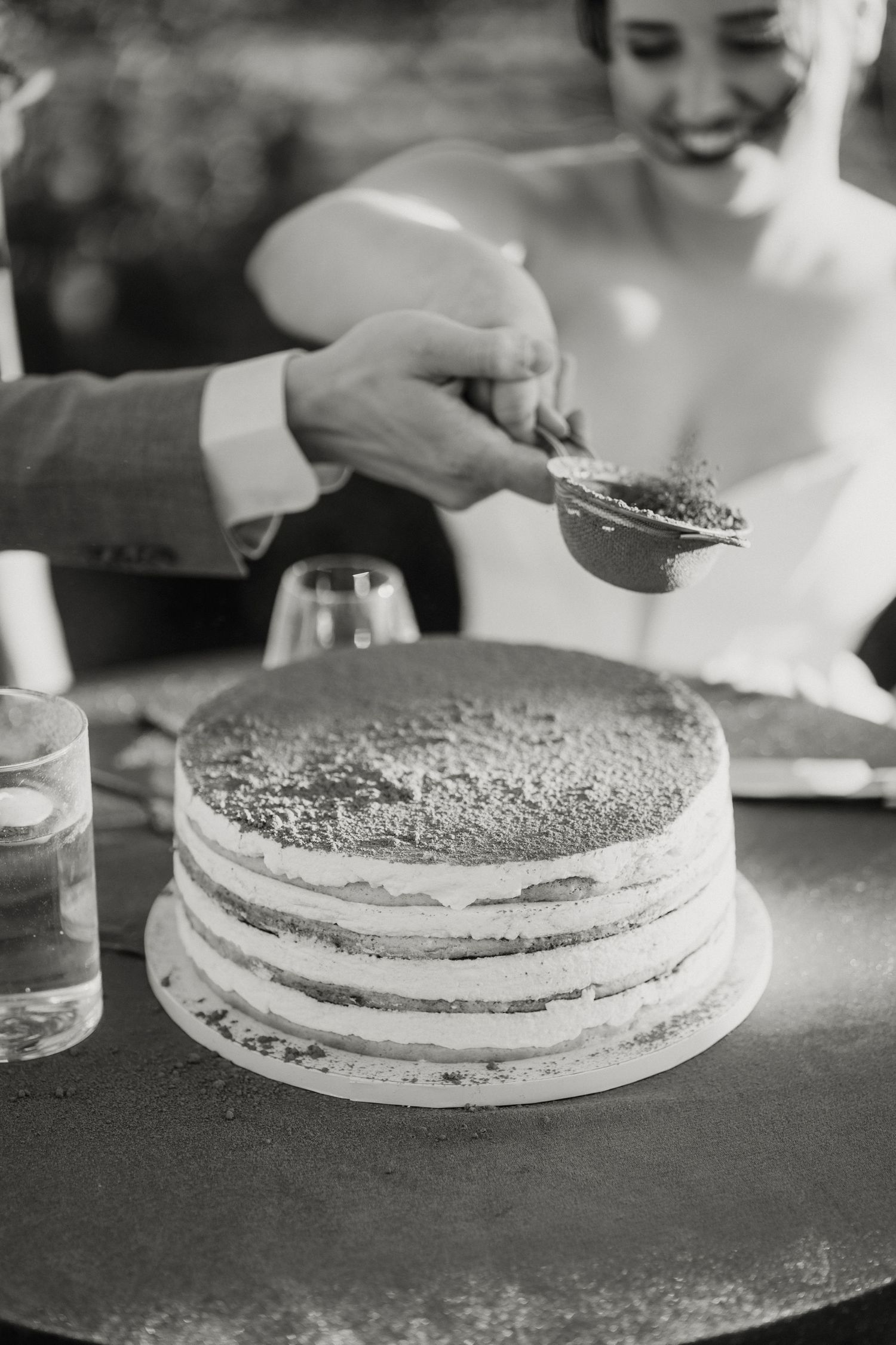 Bride and groom cut a rustic naked layered wedding cake in a black and white wedding reception photo.