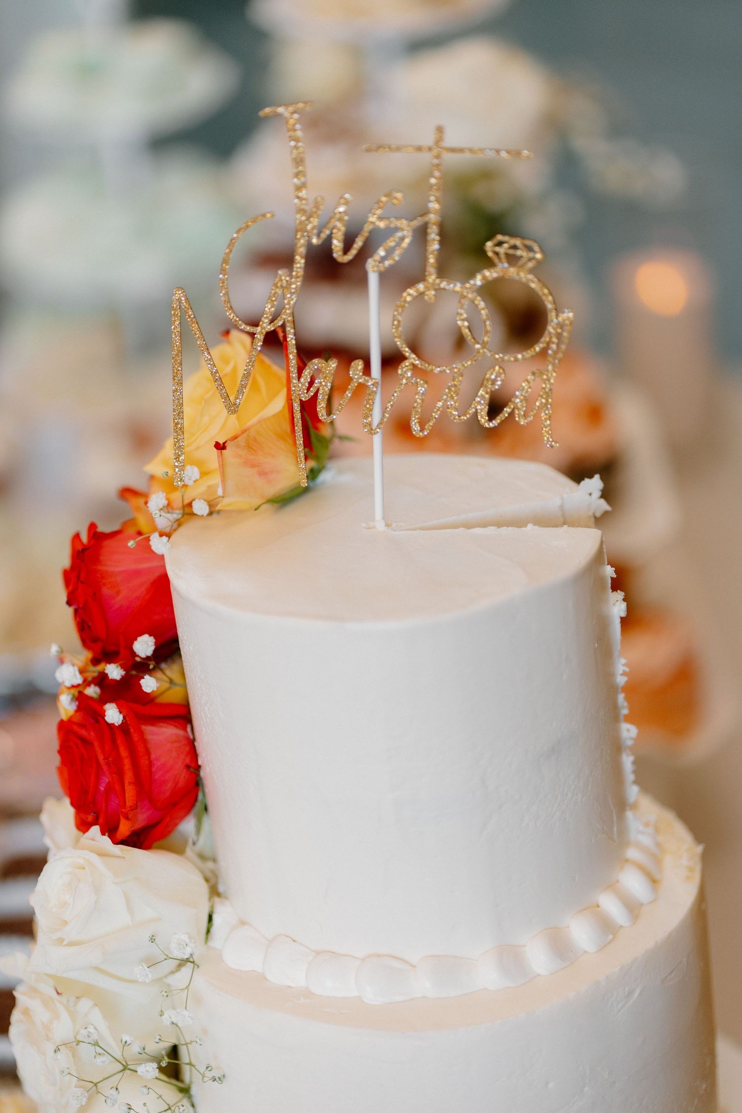 Elegant two-tier white wedding cake with Just Married topper and colorful red and yellow roses.