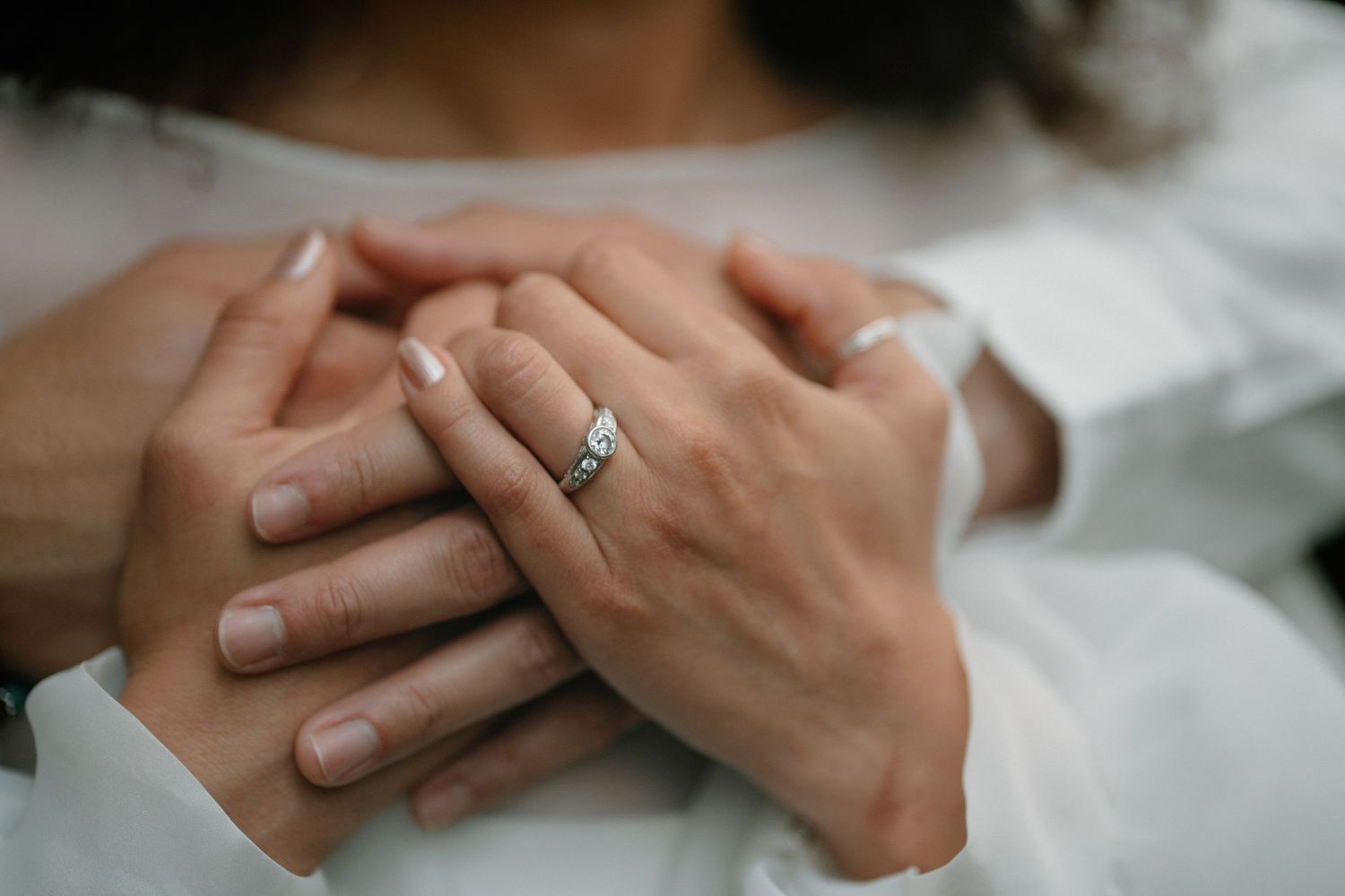 Close-up of couple's hands intertwined, bride wearing a delicate diamond engagement ring in white setting.