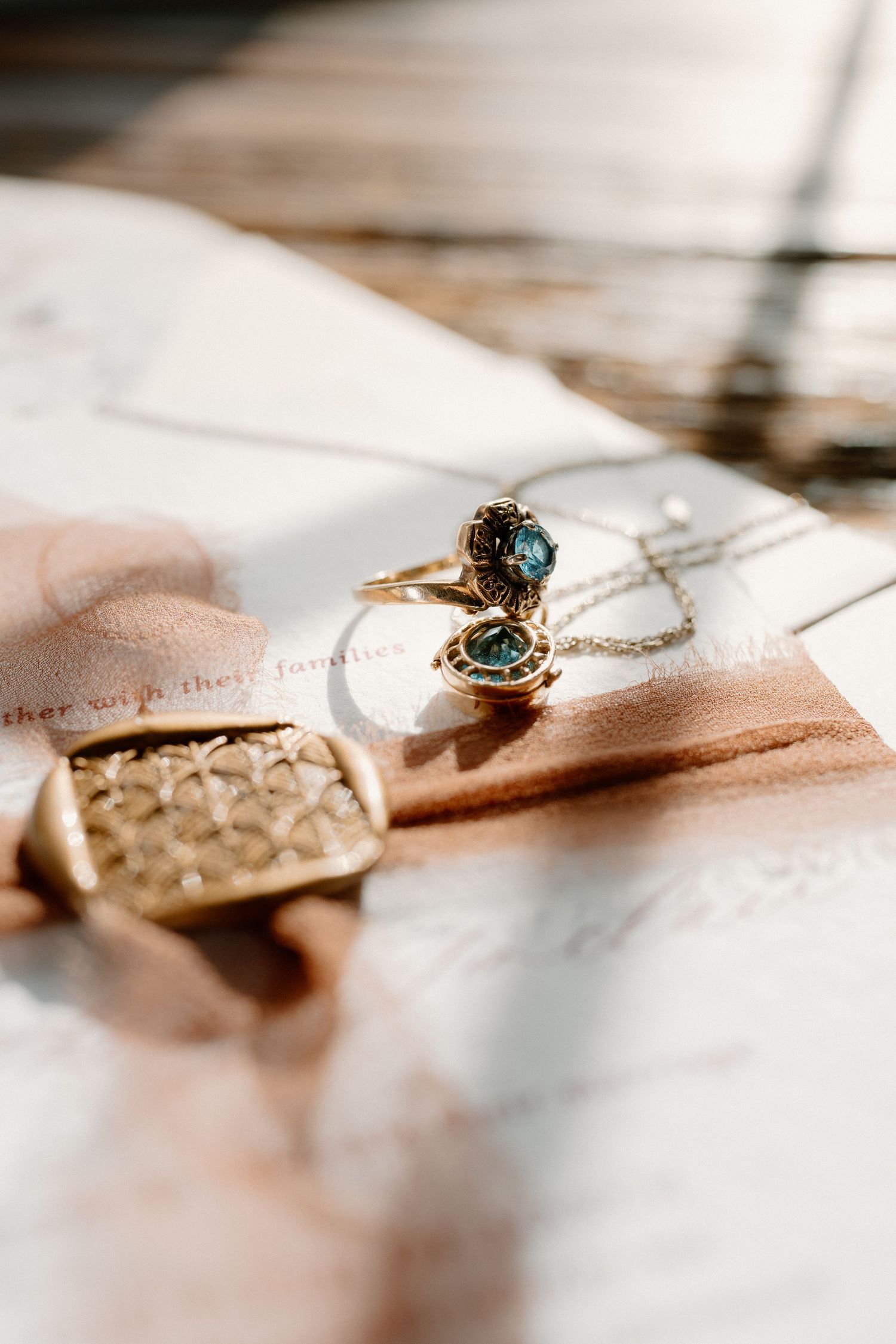 Gold ring with blue gemstone and delicate necklace displayed on wedding stationery with soft natural light.