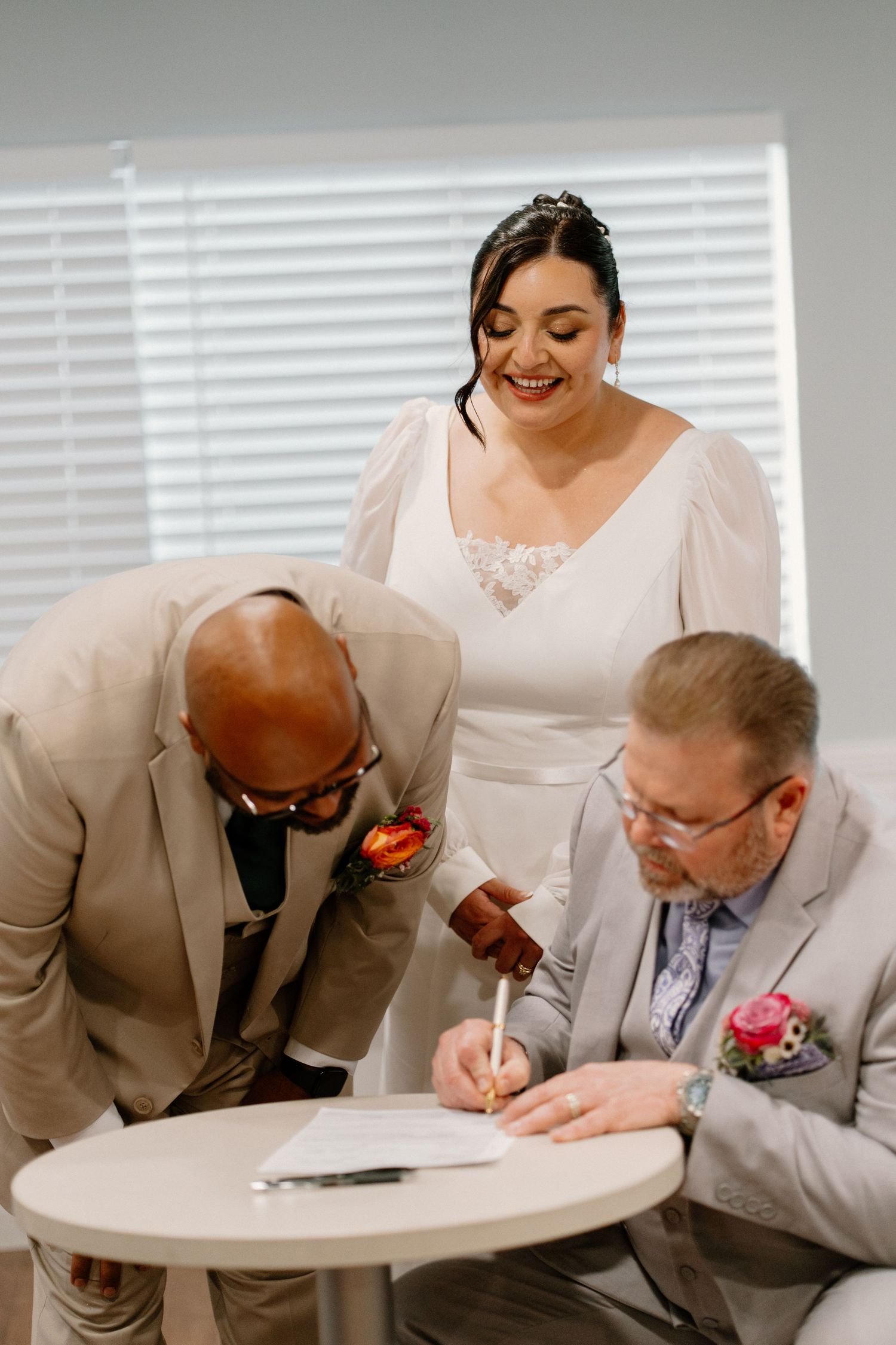 Bride and groom signing wedding certificate with officiant at small white table during ceremony.