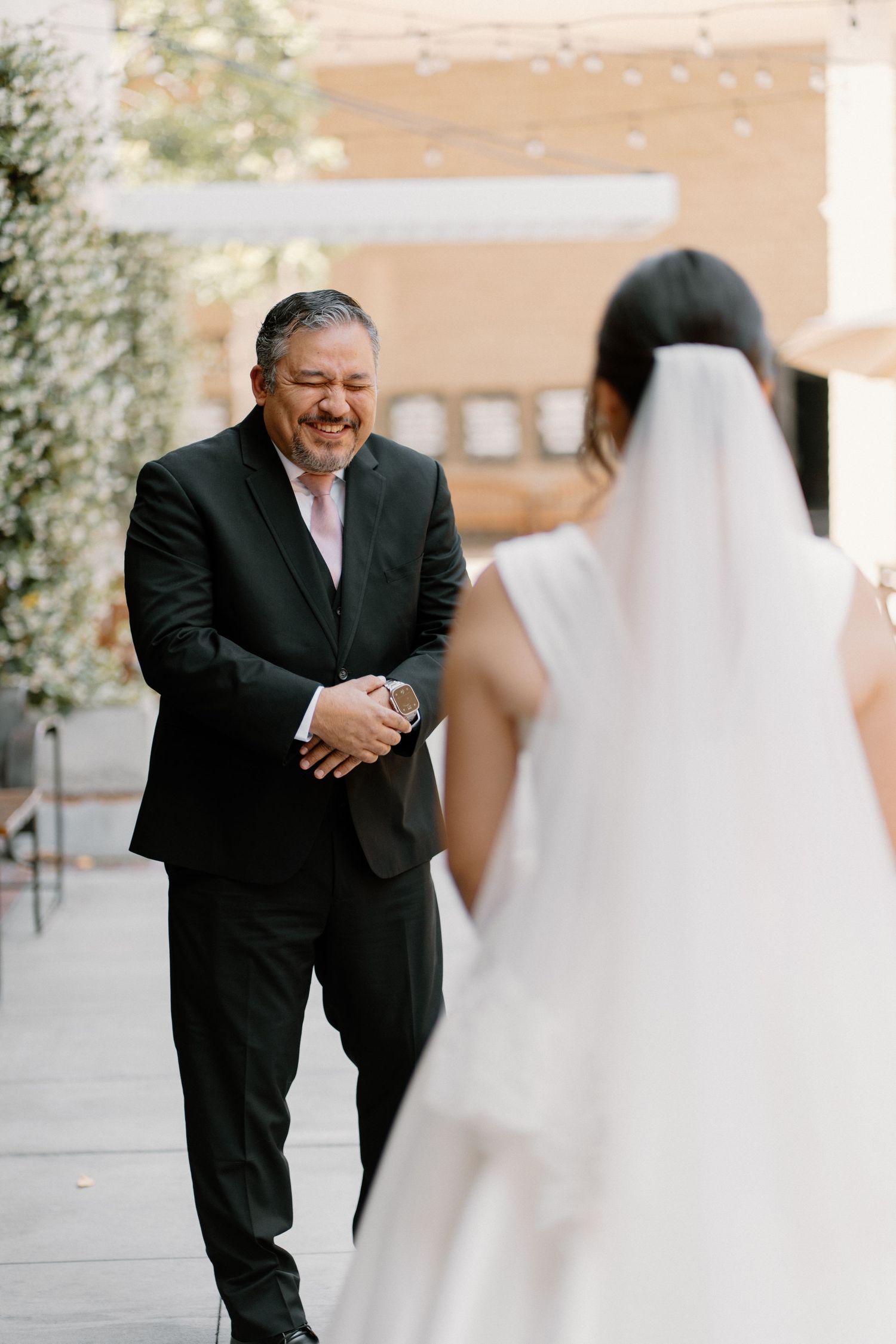Emotional father smiles with clasped hands as he sees his daughter the bride in her wedding gown for the first time.
