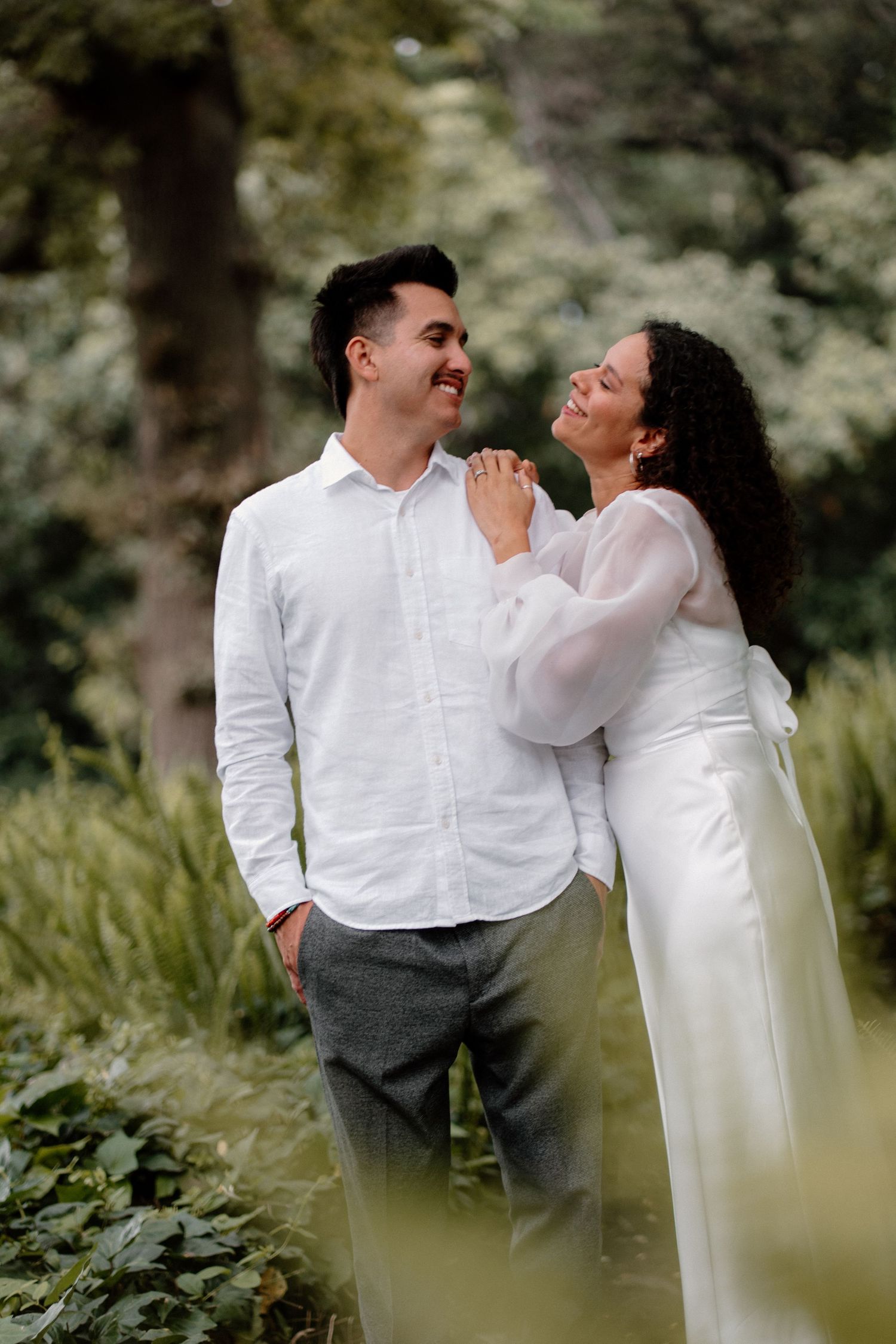 Couple smiling and gazing at each other surrounded by lush green foliage during engagement session.