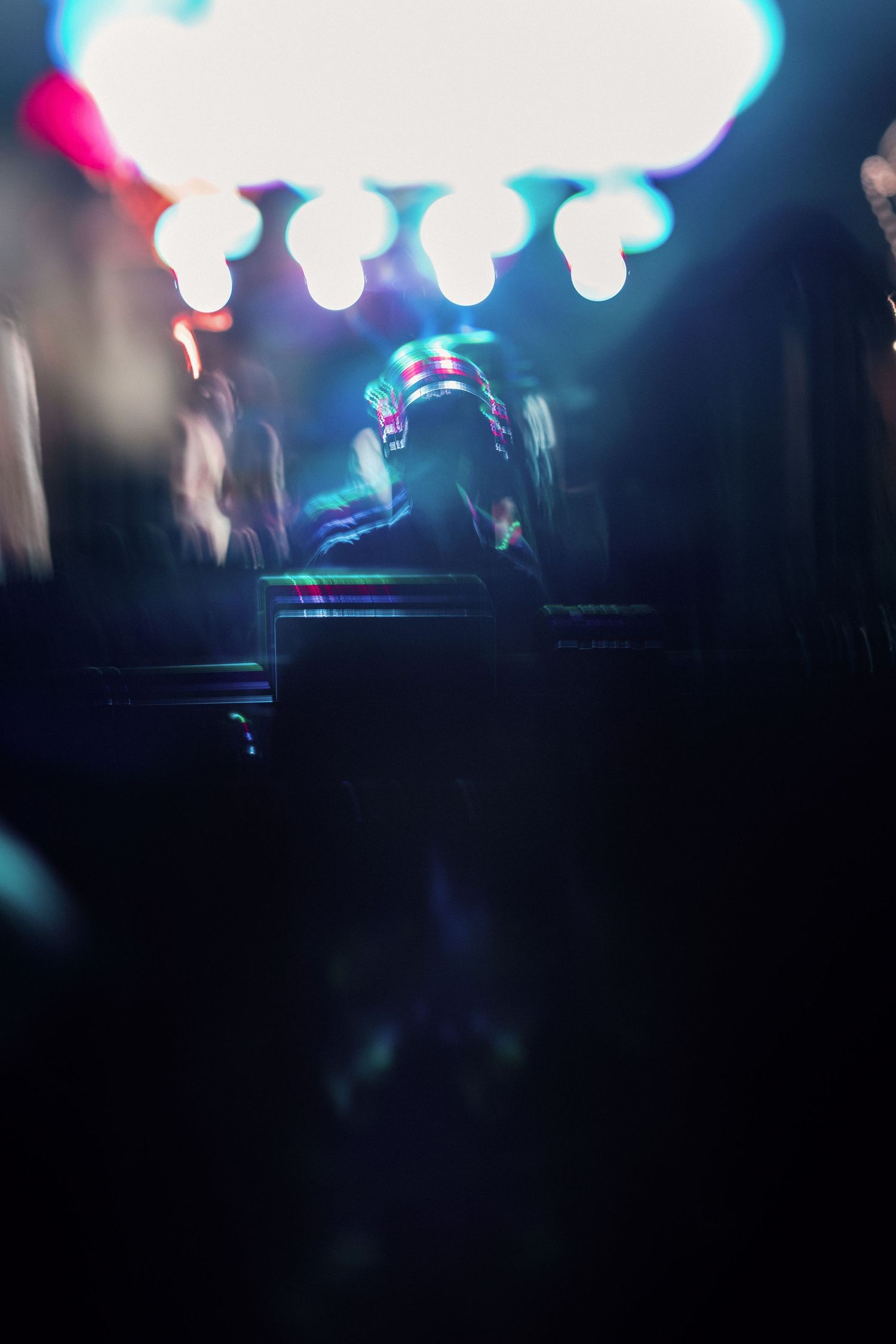 A DJ wearing an illuminated helmet performs at a dark nightclub with colorful stage lights.