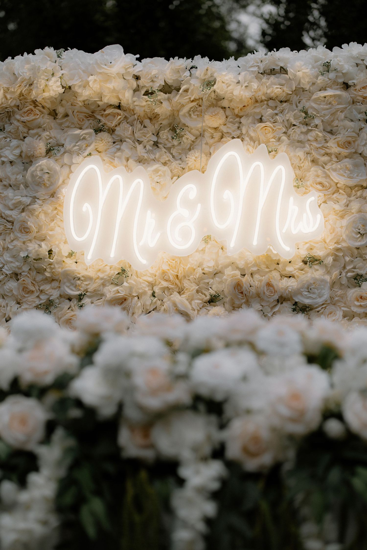 Glowing Mr & Mrs neon sign surrounded by white roses and hydrangeas at a romantic wedding reception.