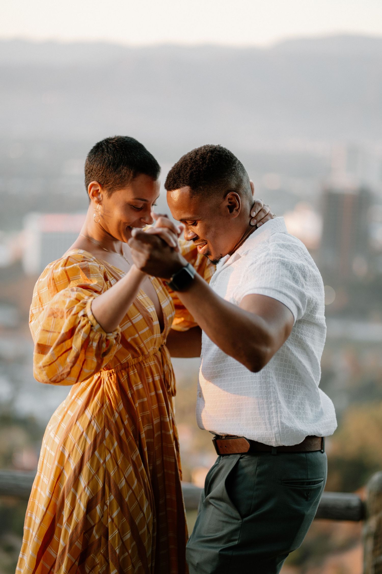 A couple holds hands and leans in close during a romantic golden hour engagement session outdoors.