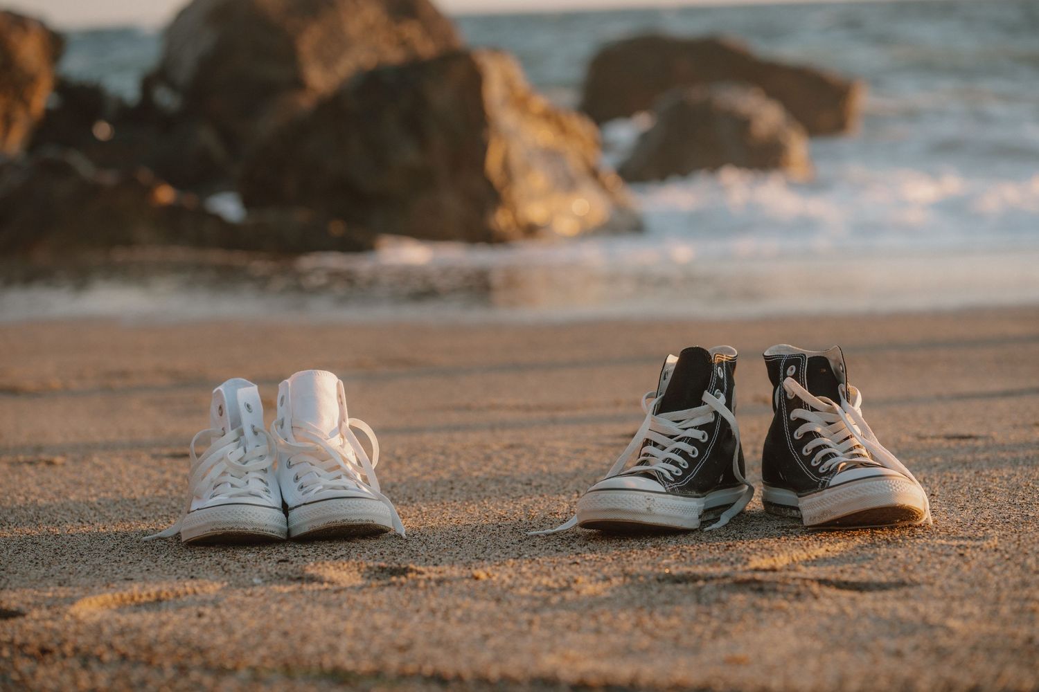Two pairs of sneakers on sandy beach at sunset near rocks.