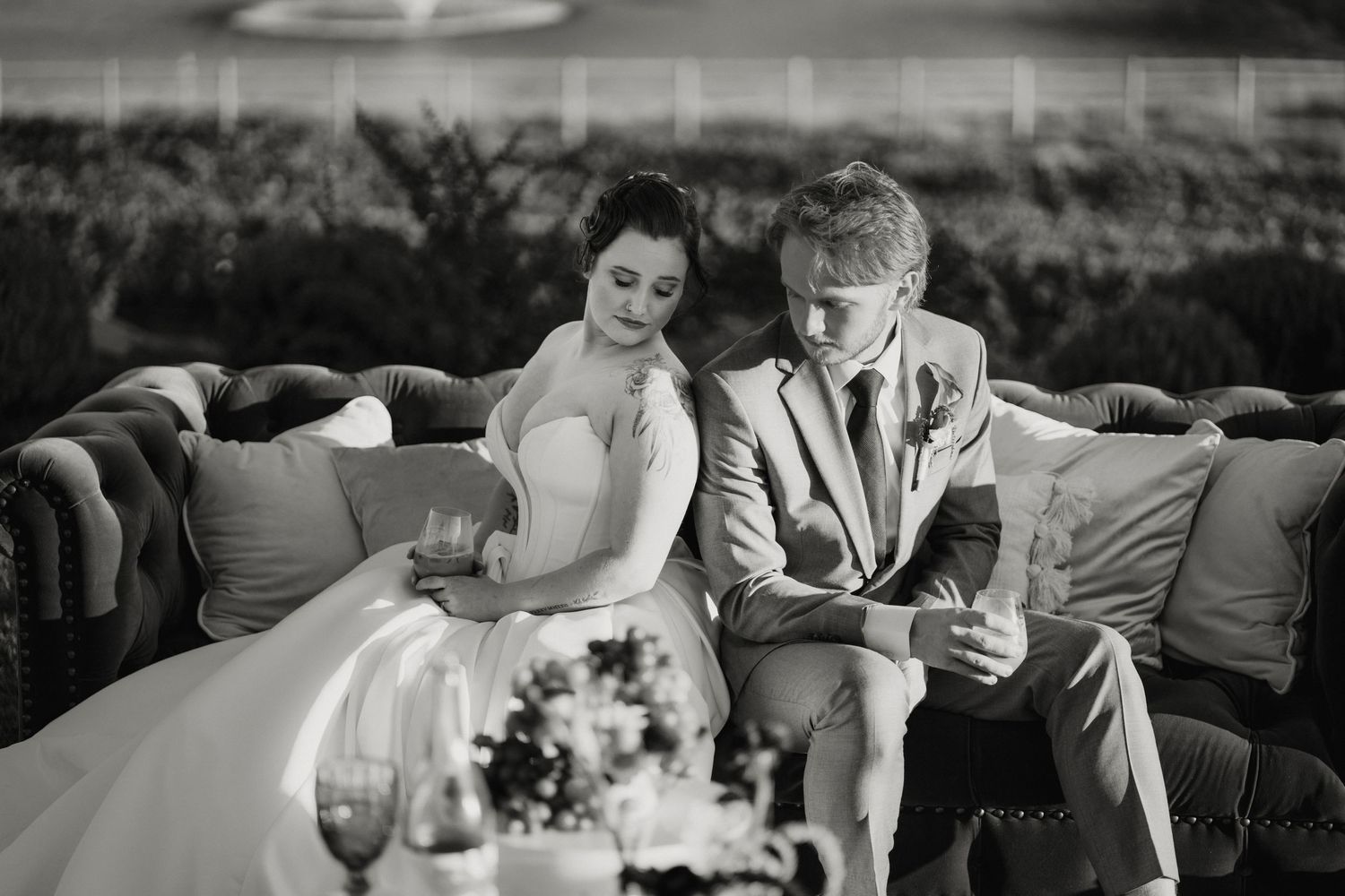 Black and white photo of bride and groom sitting together on a couch at their wedding reception.