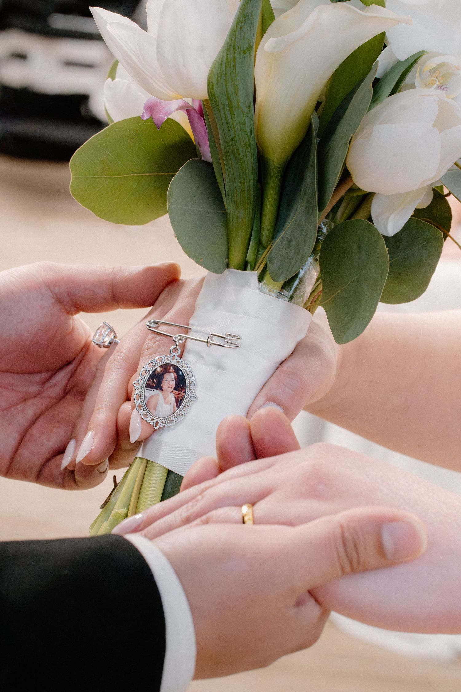 Close-up of bridal bouquet with memorial photo charm pinned to white ribbon held by couple.
