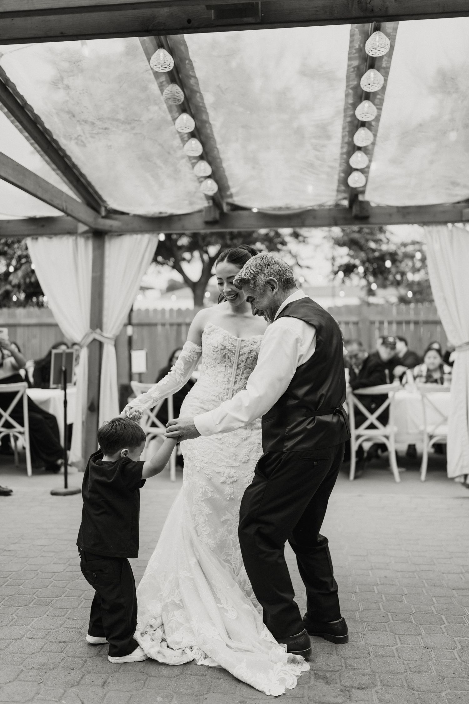 Black and white photo of bride and groom dancing with a young child at their wedding reception.