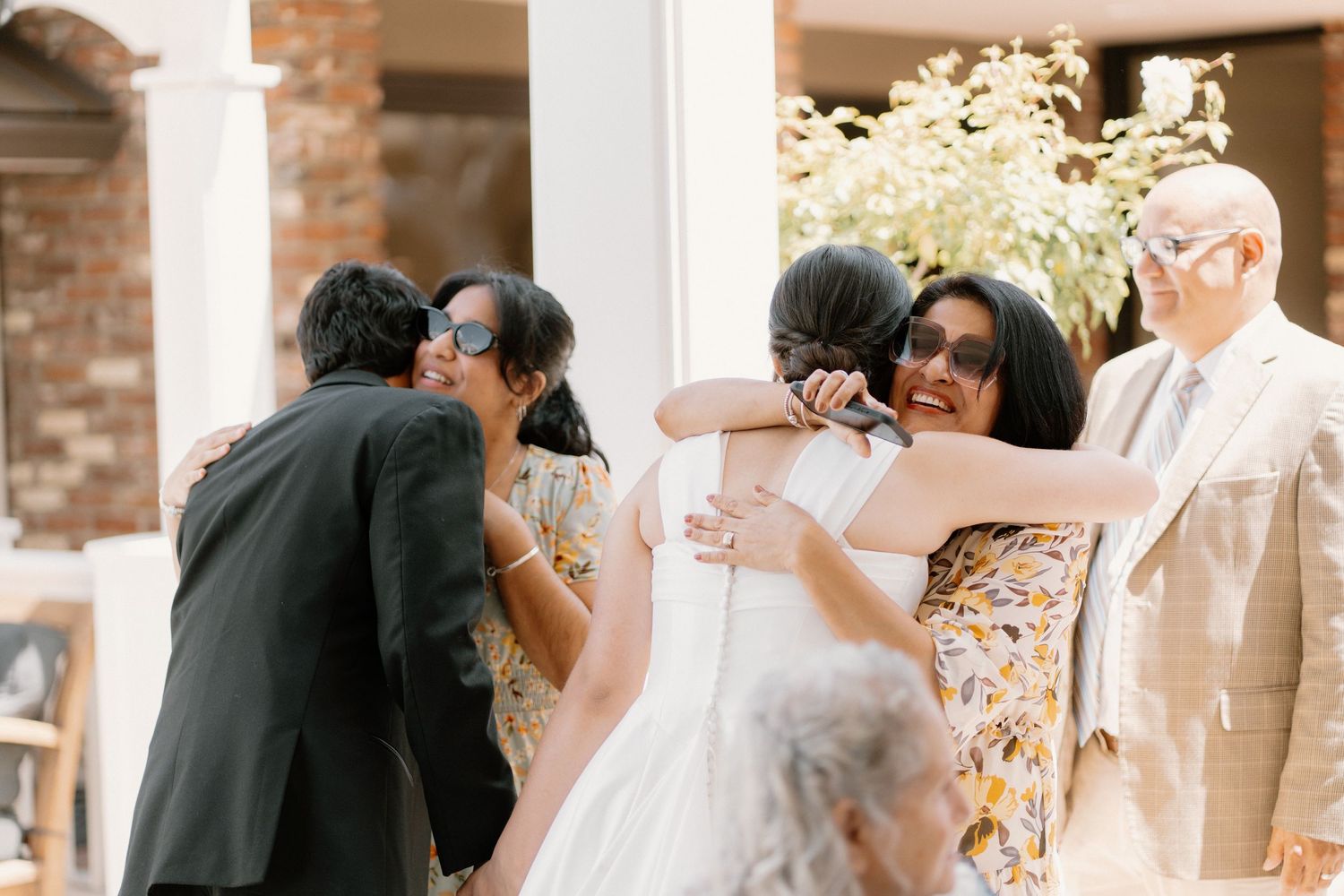 Bride receives warm hugs from family members after outdoor wedding ceremony.
