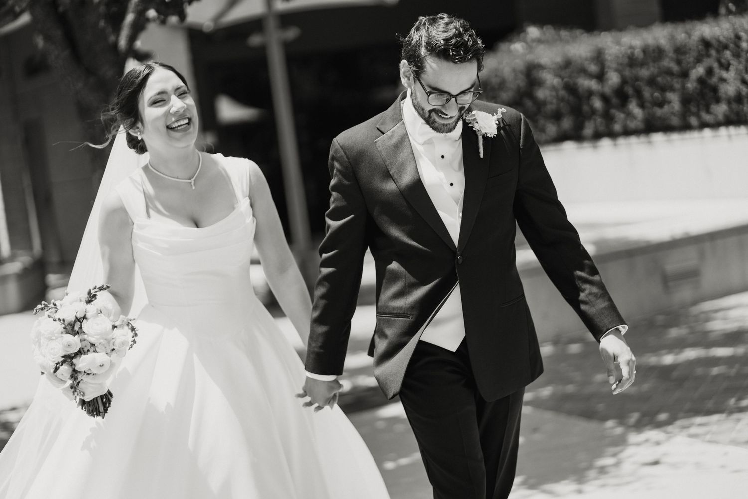 Happy bride and groom walking hand in hand in black and white wedding photo.