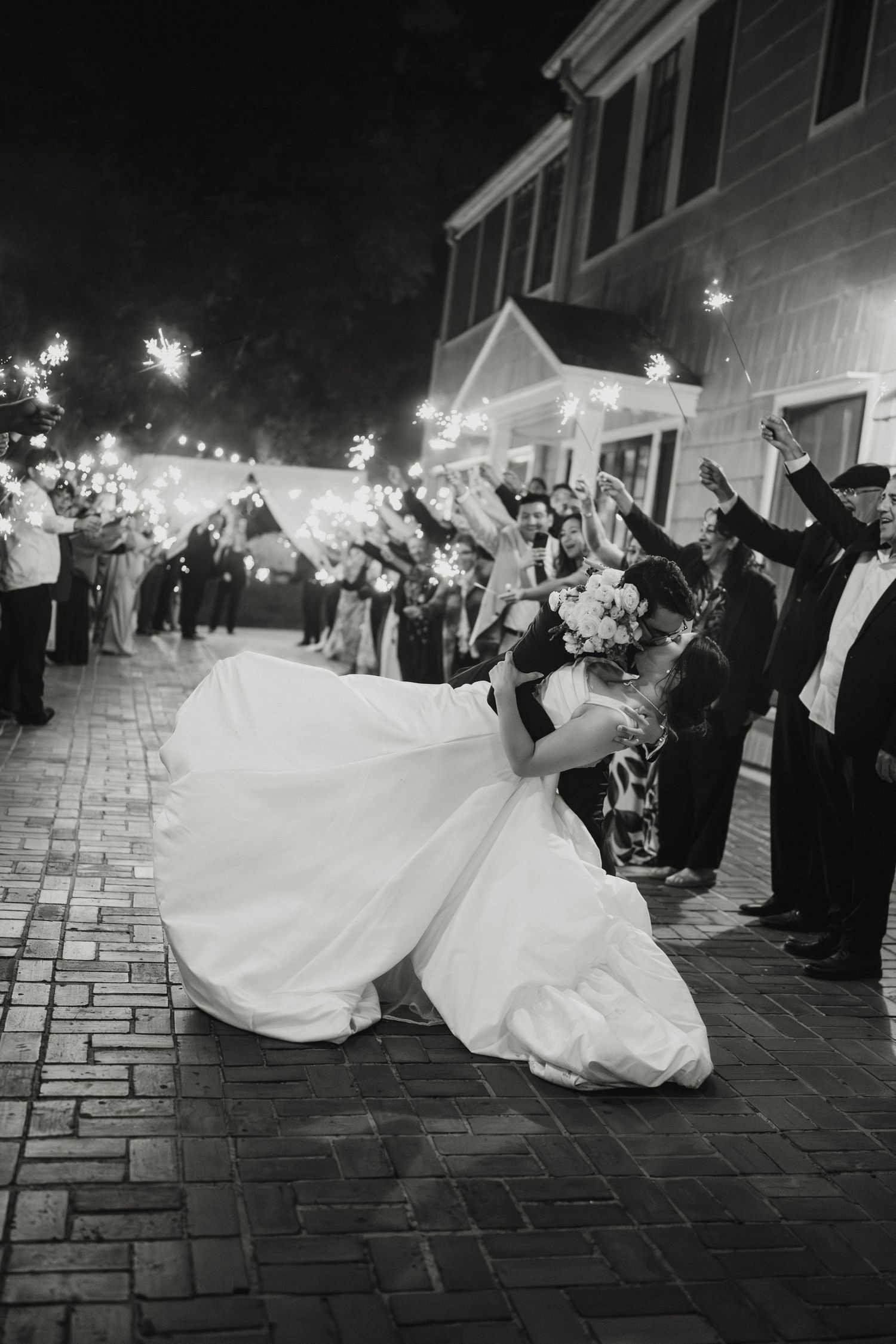 Bride and groom share romantic dip kiss during sparkler send-off exit lined with cheering guests.