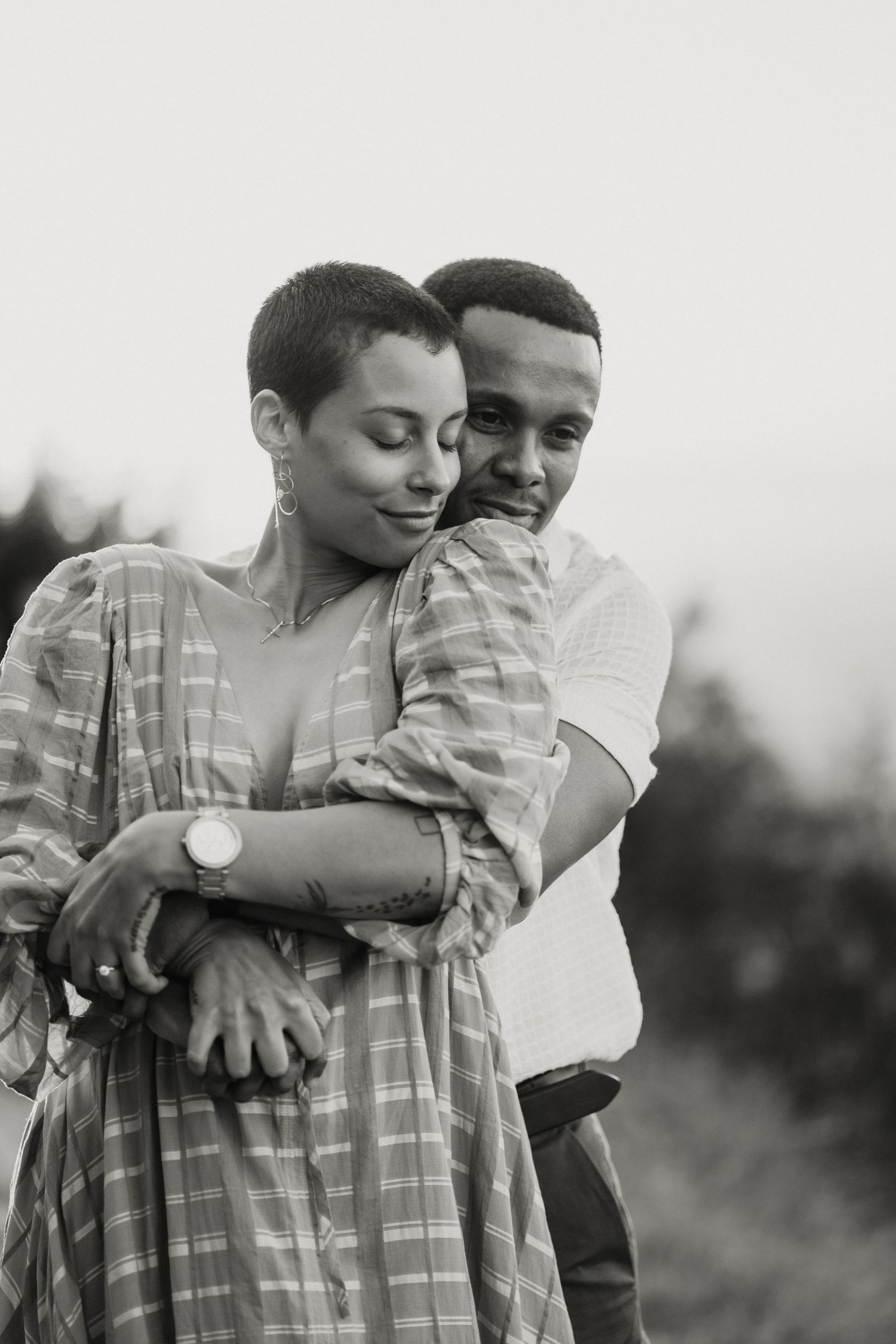 Black and white portrait of a man tenderly embracing a woman with a short haircut from behind.