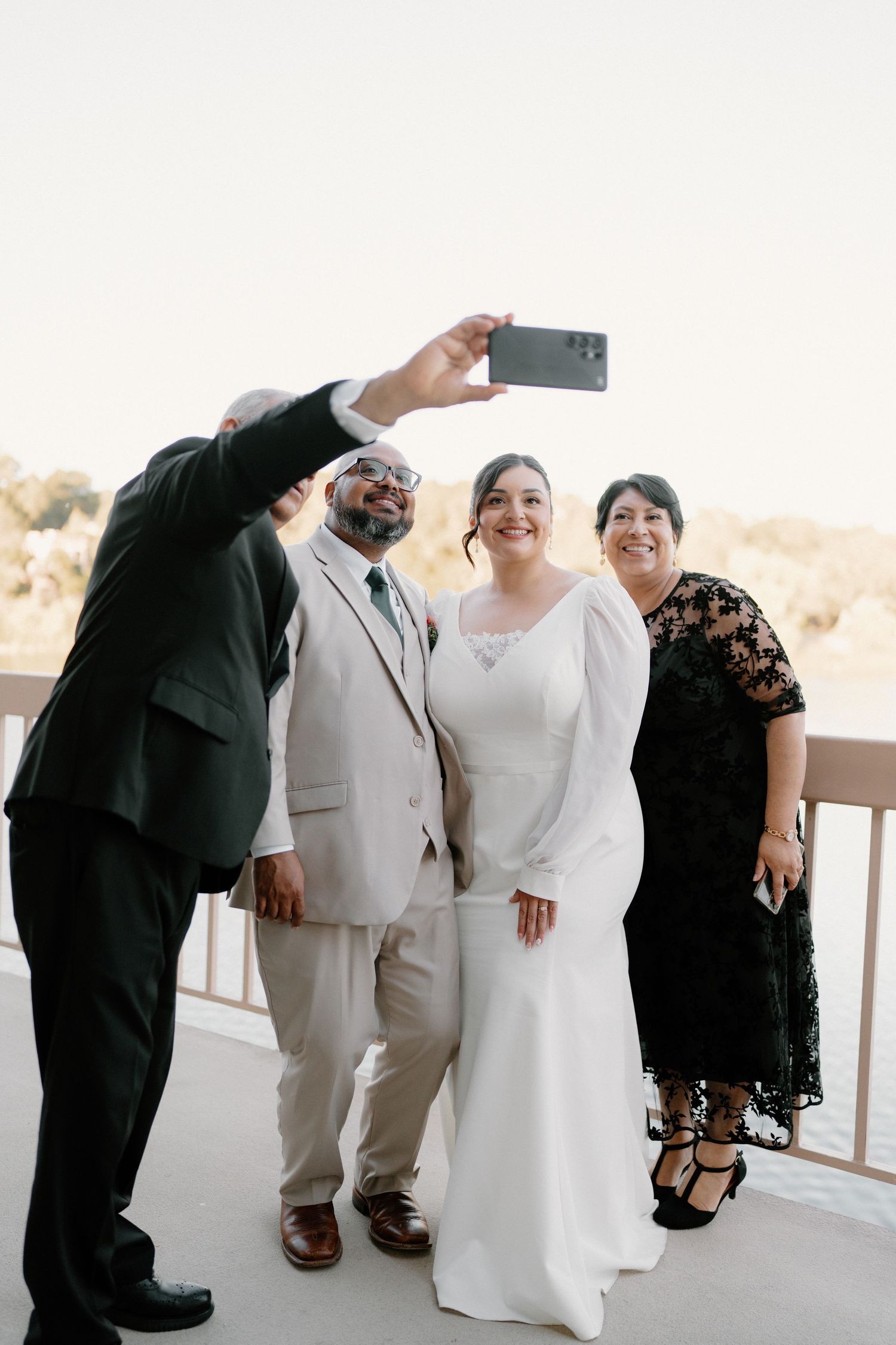 Bride, groom, and two guests taking a group selfie on an outdoor balcony at a wedding reception.