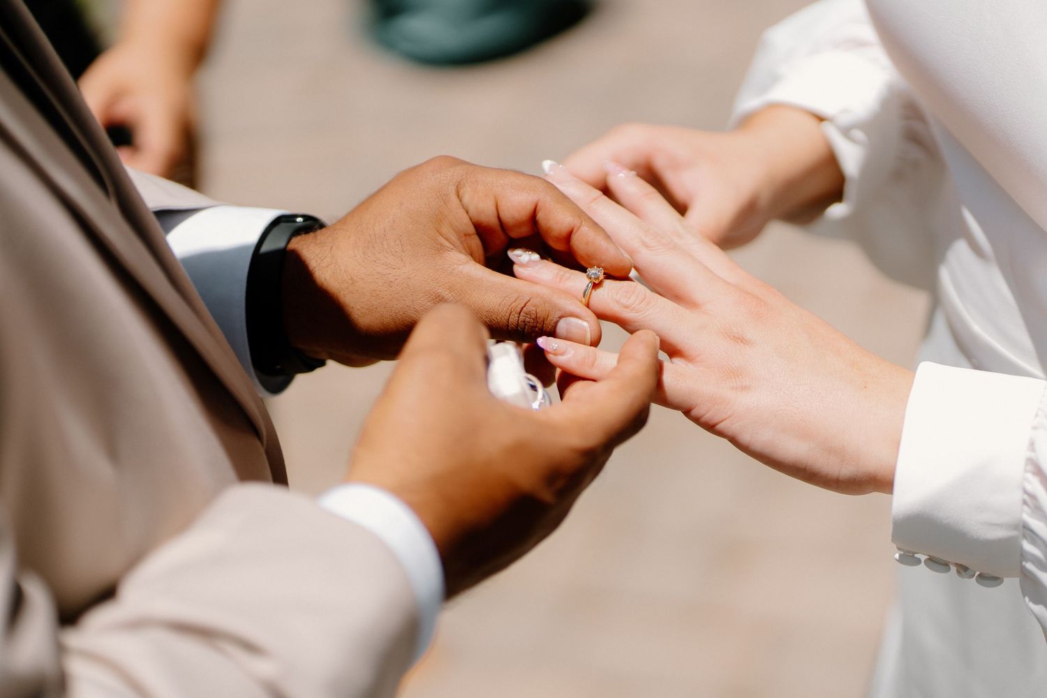 Groom placing a wedding ring on brides finger during a ceremony, close-up of hands showing interracial couple.