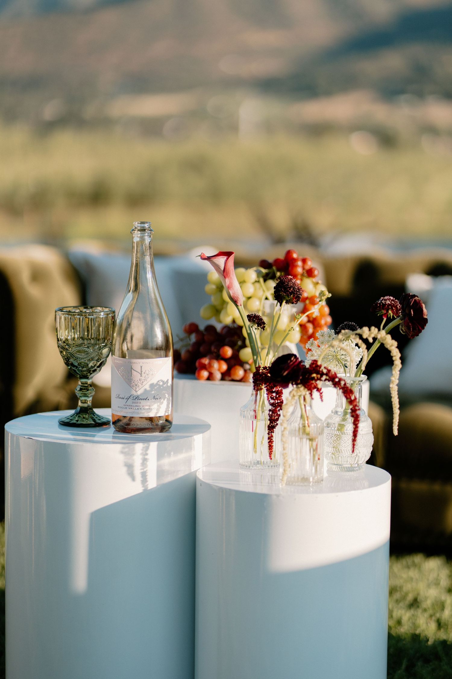 Elegant outdoor wedding display with wine bottle and burgundy floral arrangements.