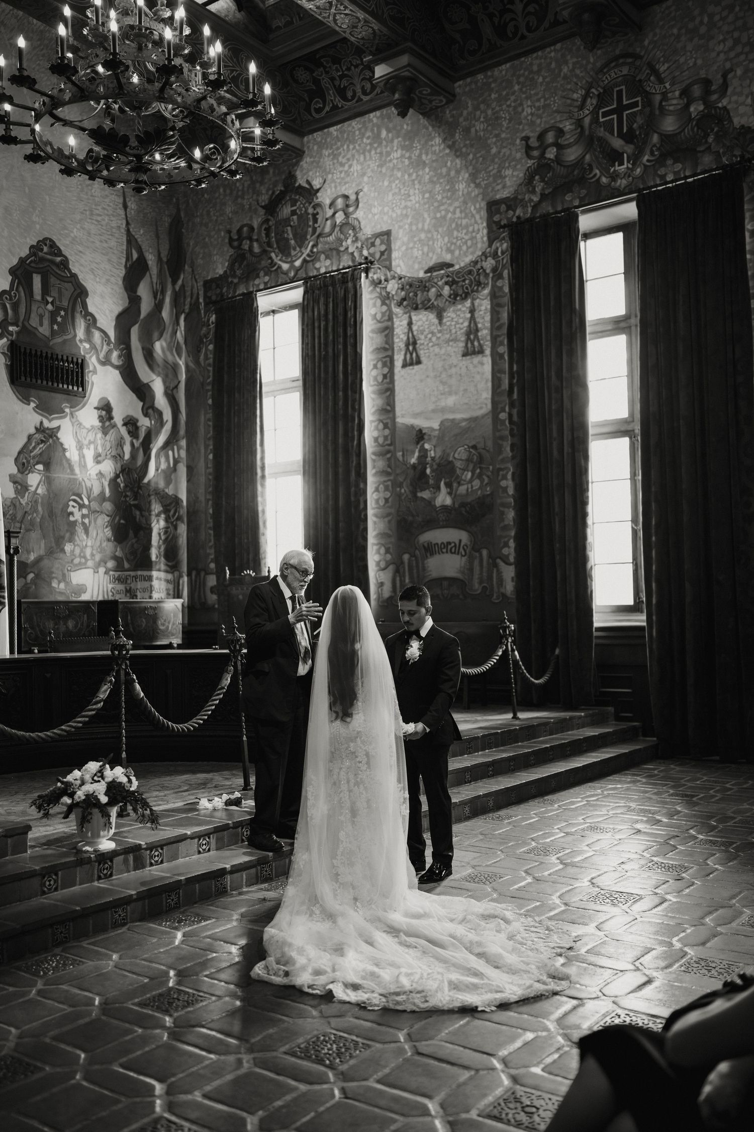 Black and white photo of bride and groom at wedding altar in ornate historic venue with mosaic walls.