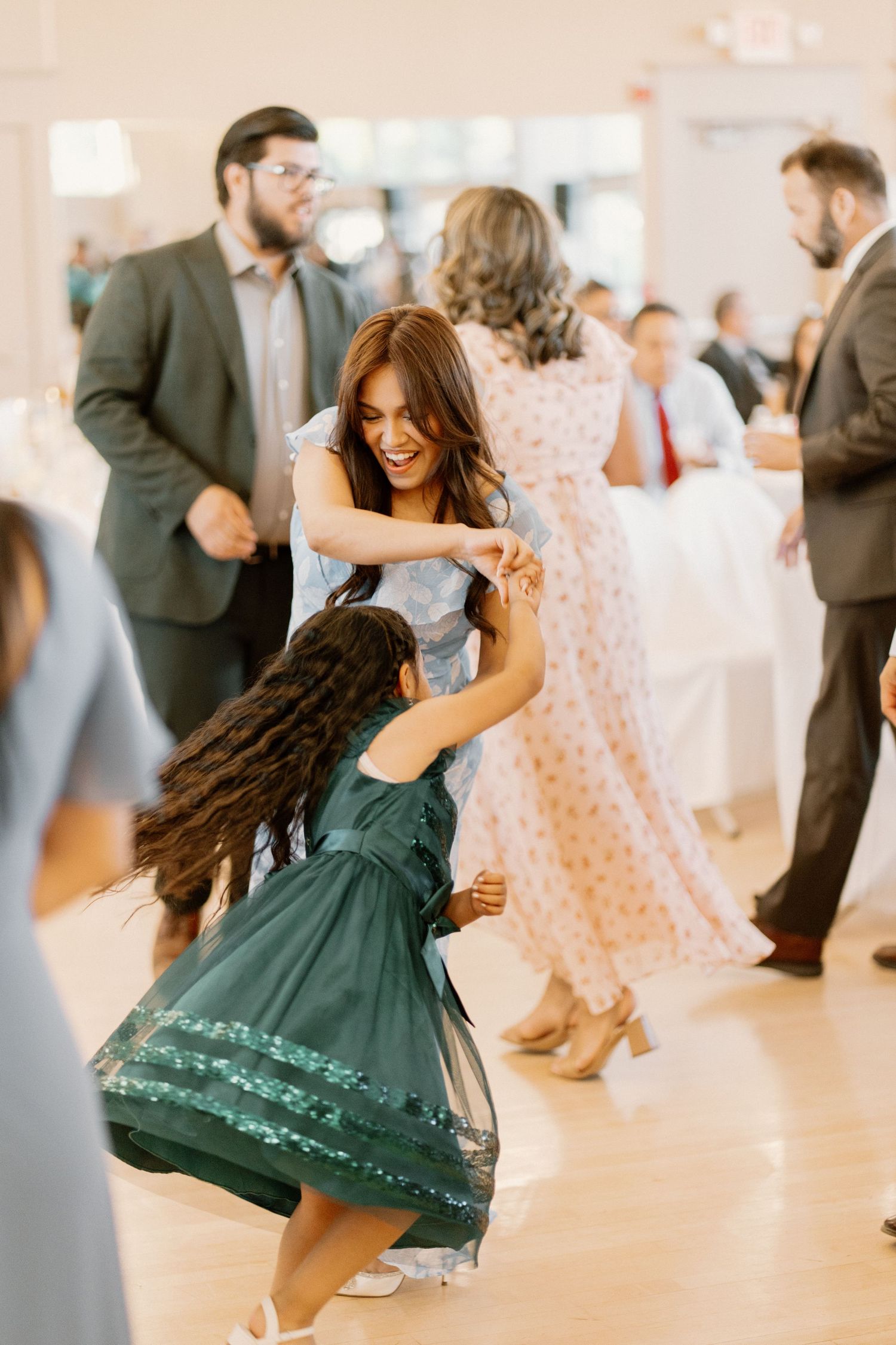 Joyful woman in blue dress dancing with young girl in green dress at wedding reception.