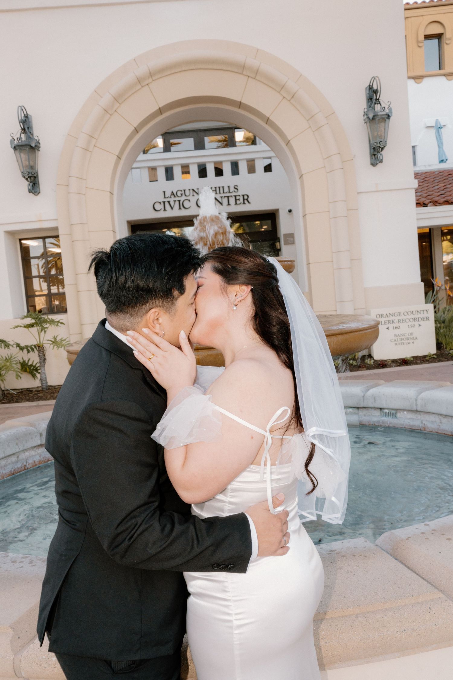 Newlyweds kissing in front of Laguna Hills Civic Center fountain after wedding.