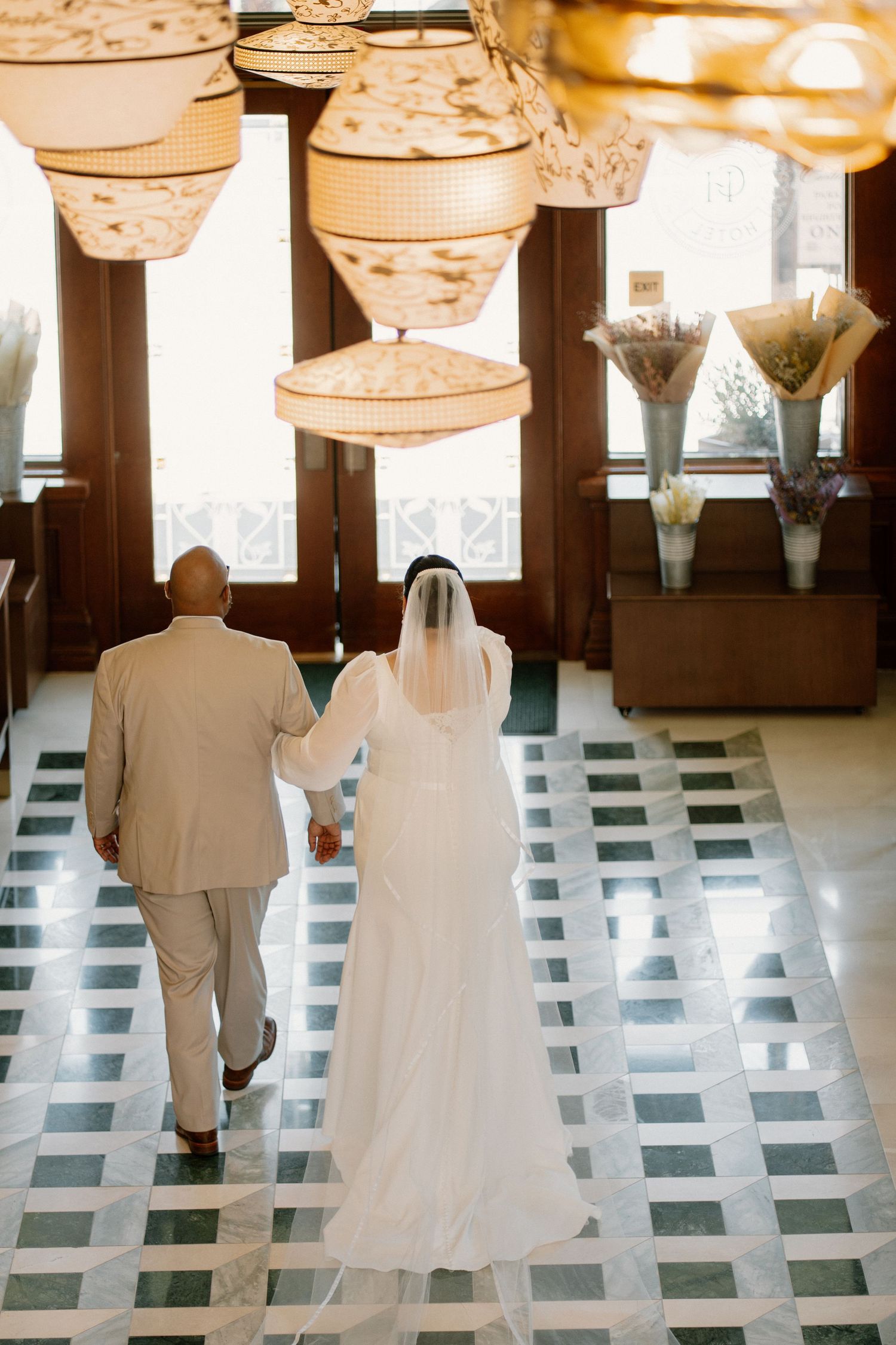 Bride and groom walk hand in hand through elegant venue with decorative hanging lanterns.