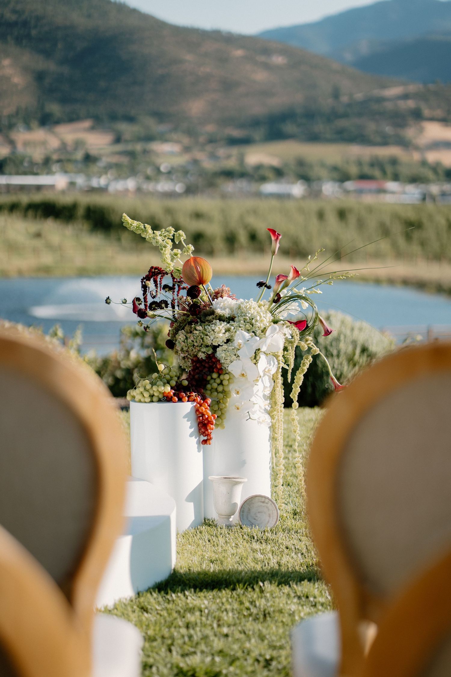 Elegant outdoor wedding ceremony aisle with floral arrangements and mountain lake backdrop.