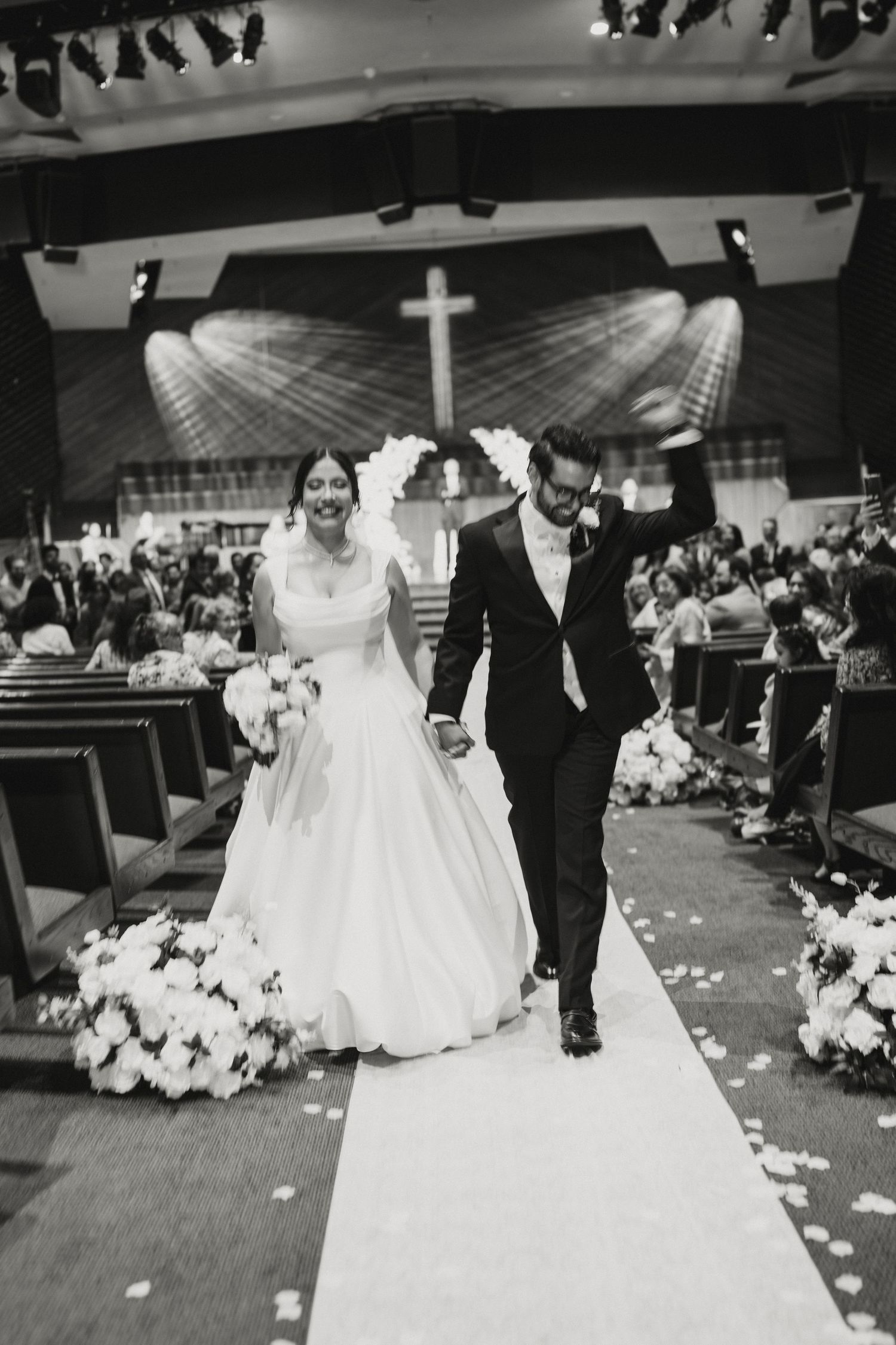 Black and white photo of newlyweds joyfully walking down the aisle after church wedding ceremony.
