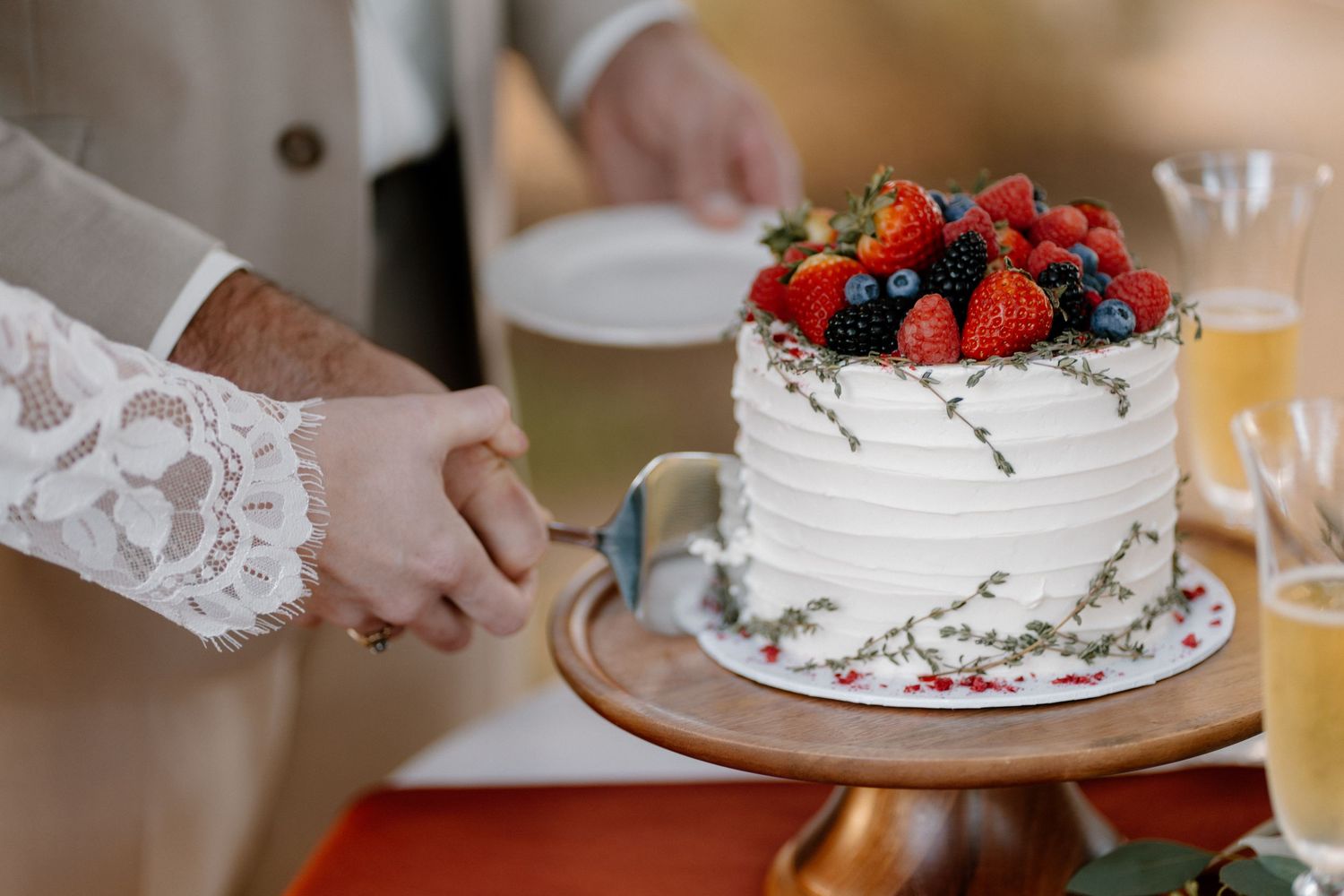 Bride and groom cut a elegant white wedding cake topped with fresh strawberries and mixed berries together.