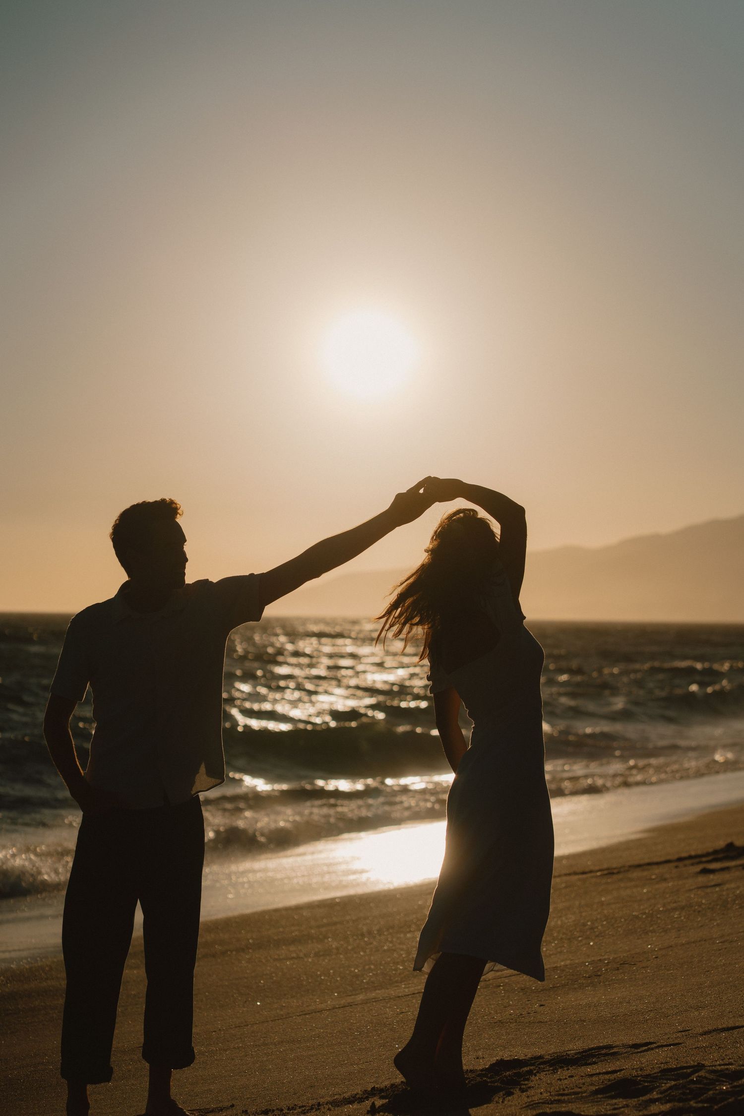 Romantic silhouette of couple dancing on beach at golden sunset by the ocean waves.