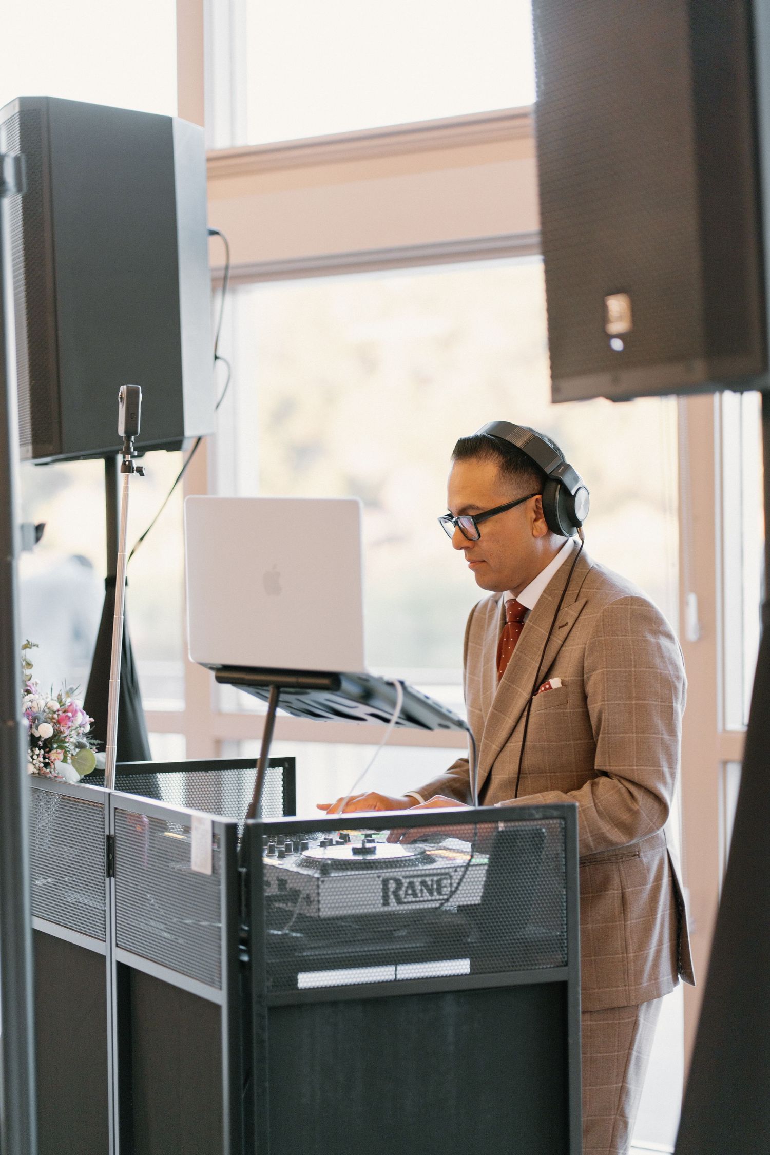 Professional DJ in plaid suit using Rane equipment and headphones at wedding reception venue.