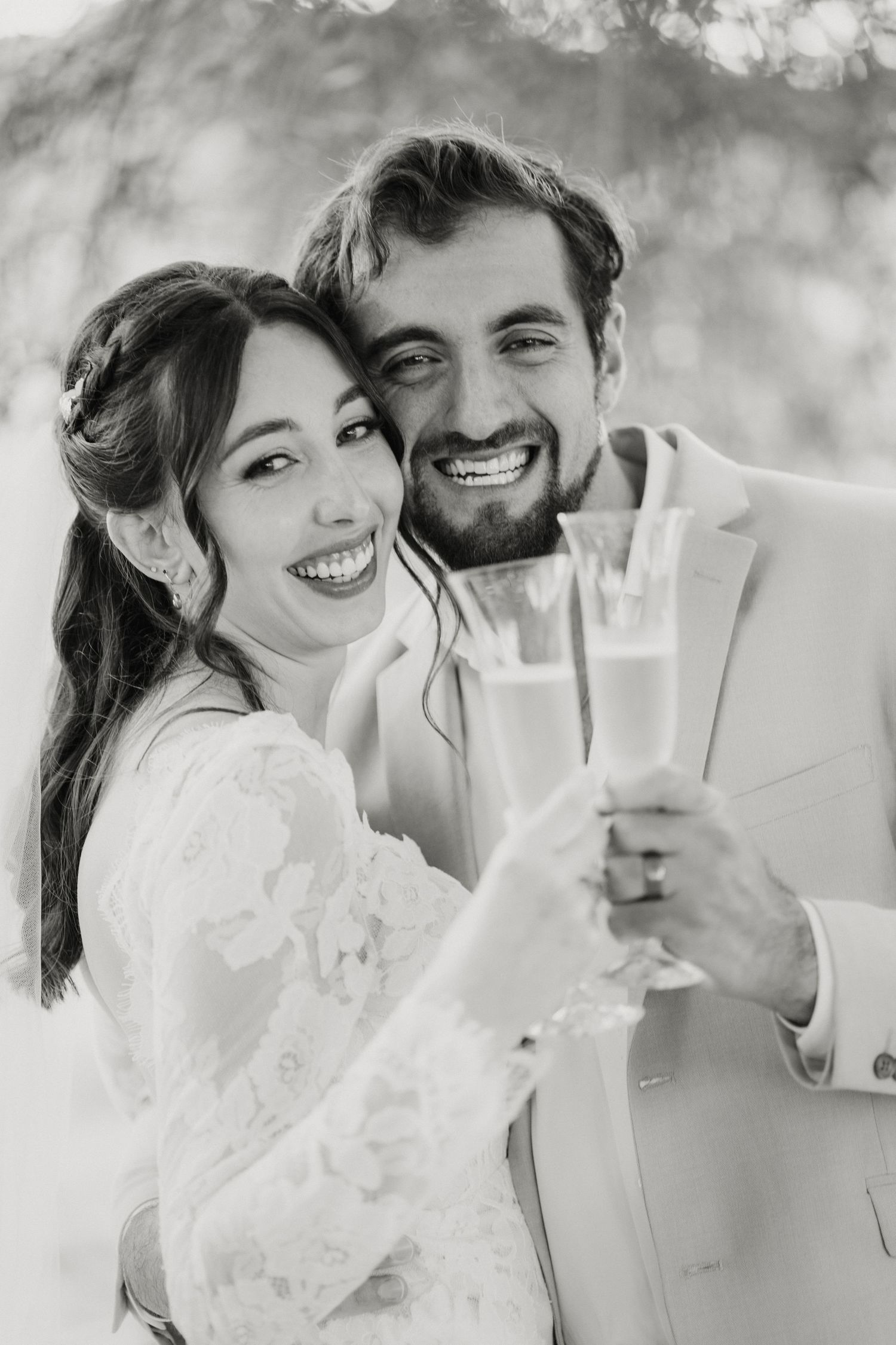 Black and white portrait of smiling bride and groom toasting with champagne glasses on their wedding day.