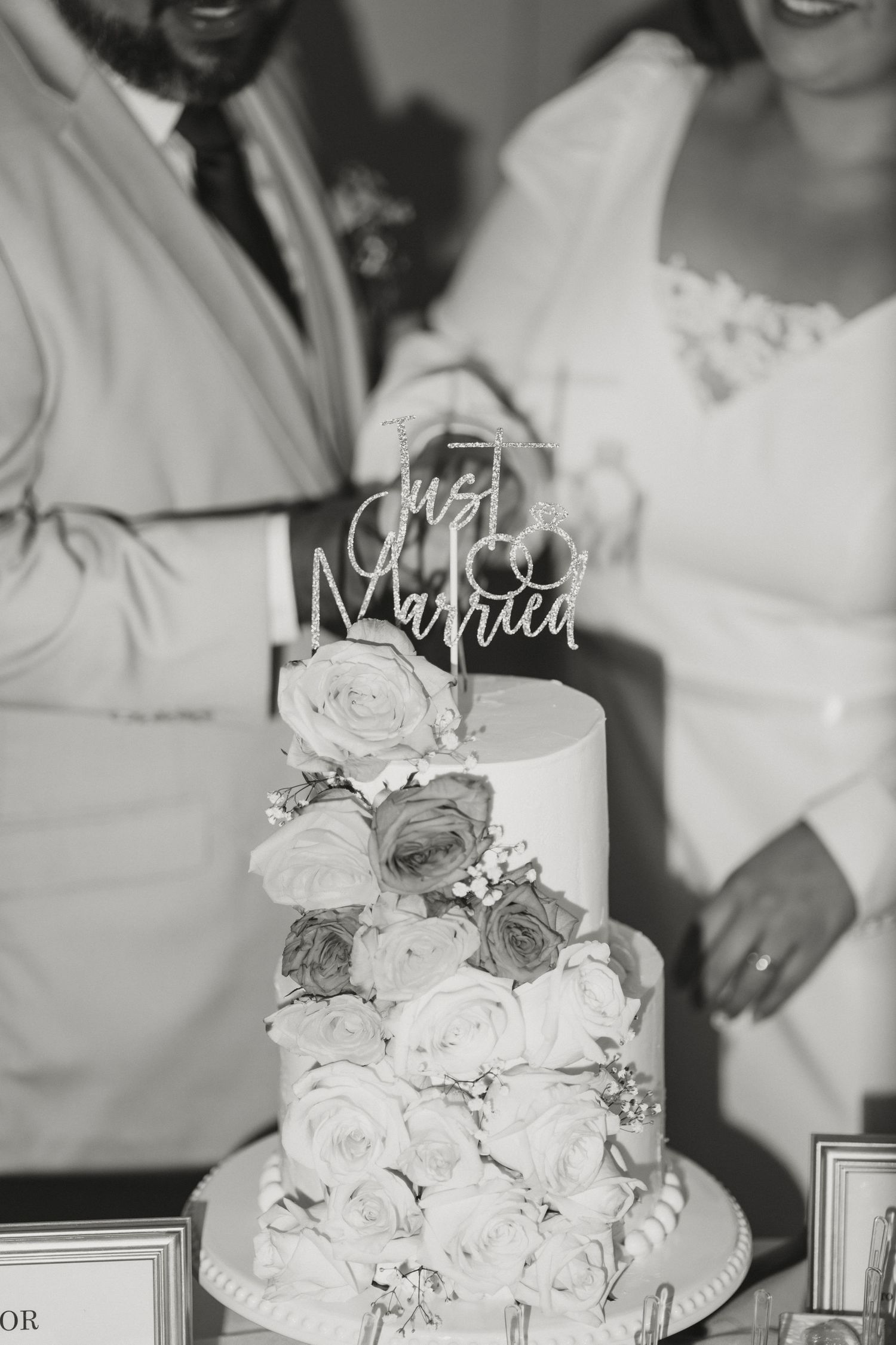 Black and white photo of a Just Married wedding cake with roses, as newlyweds prepare to cut it.