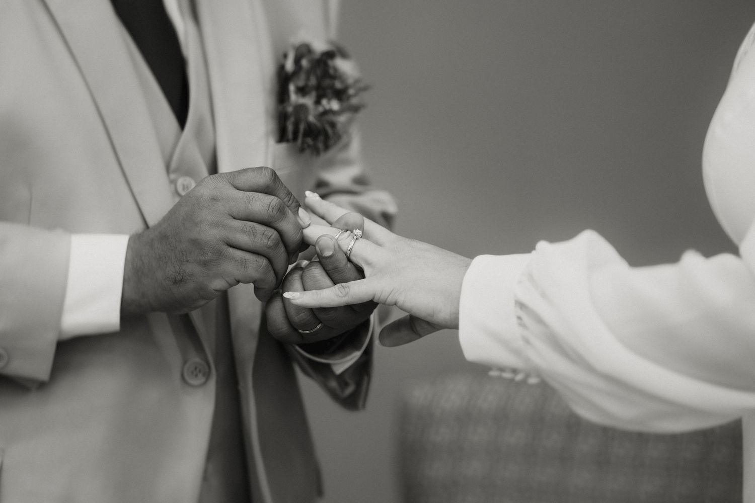 Black and white photo of a couple exchanging wedding rings during a ceremony.