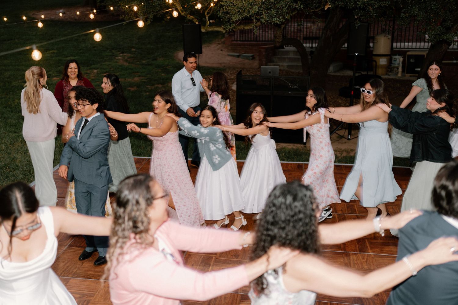 Wedding guests forming a fun chain dance line at an outdoor evening reception under string lights.