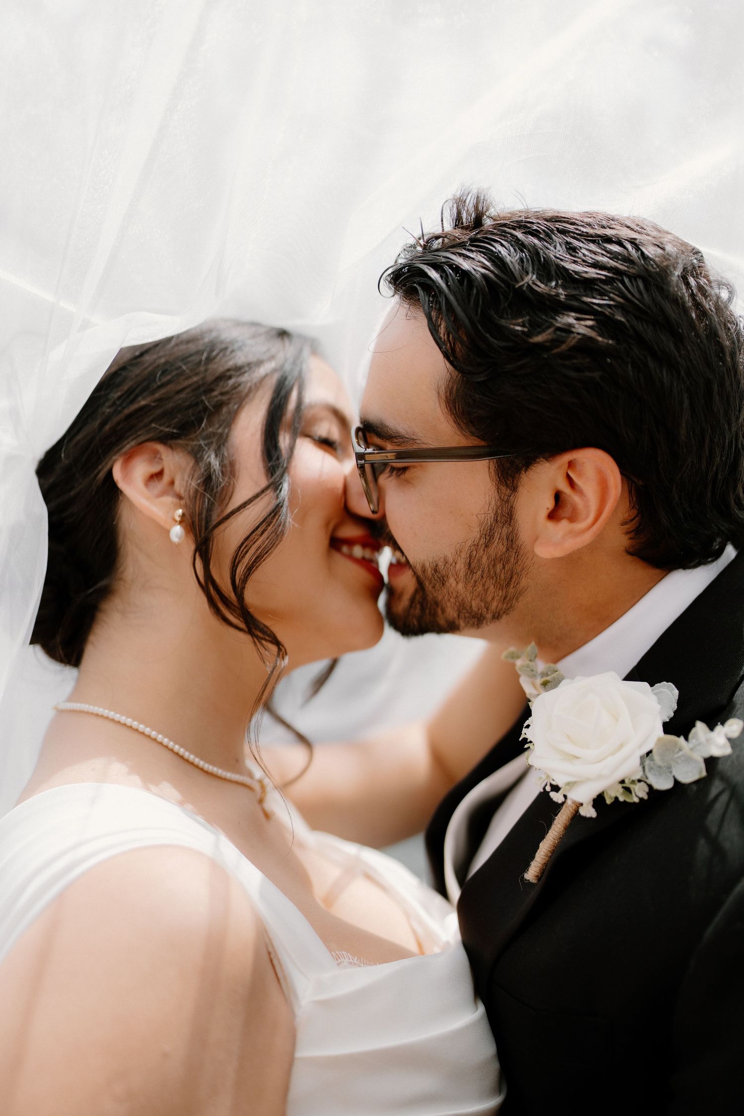Bride and groom share intimate kiss under veil at outdoor wedding ceremony.
