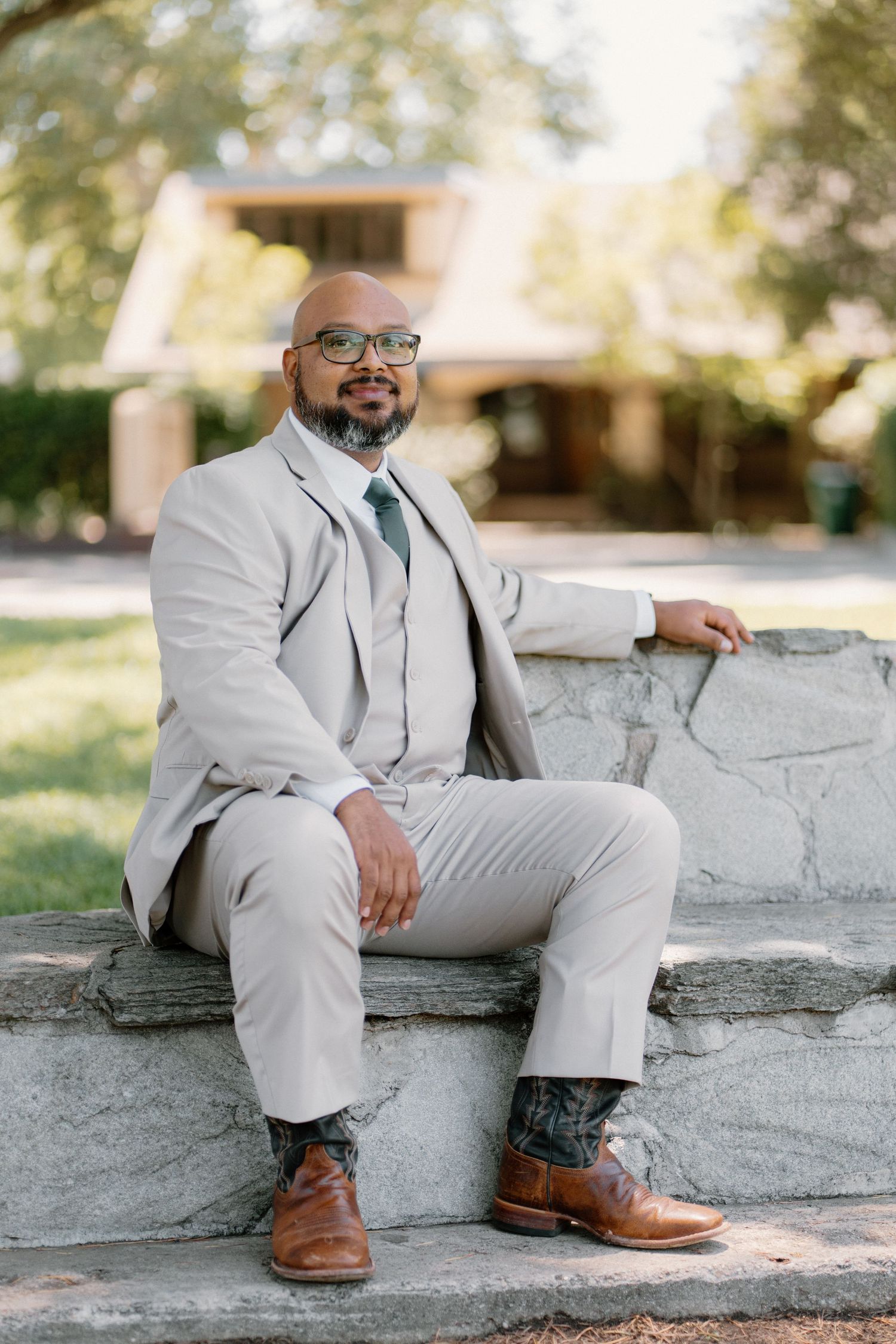 Bald man in light gray suit sitting on stone steps outdoors, wearing glasses and brown leather shoes.
