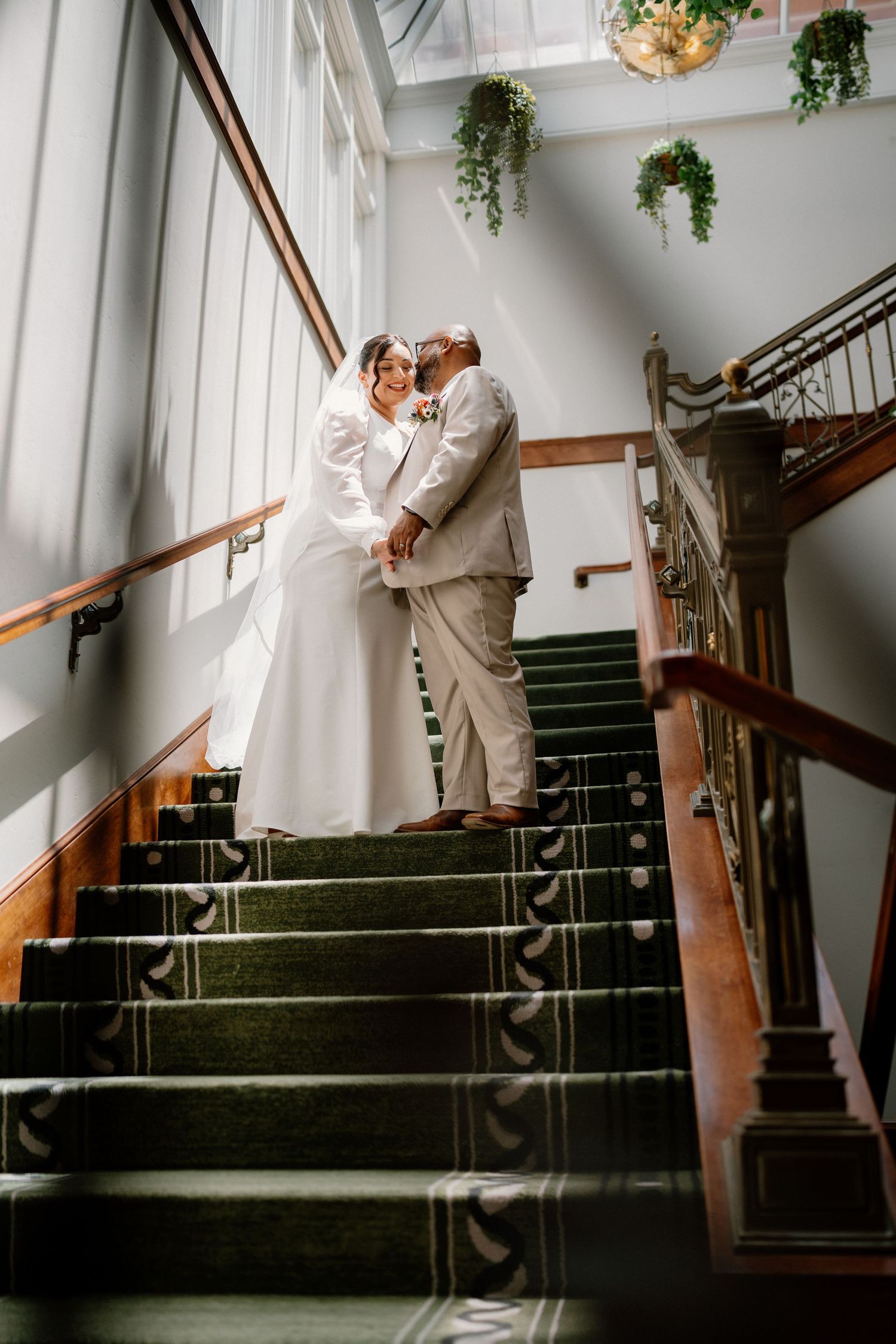 Bride and groom embrace on elegant staircase with green carpet in a classic wedding venue.